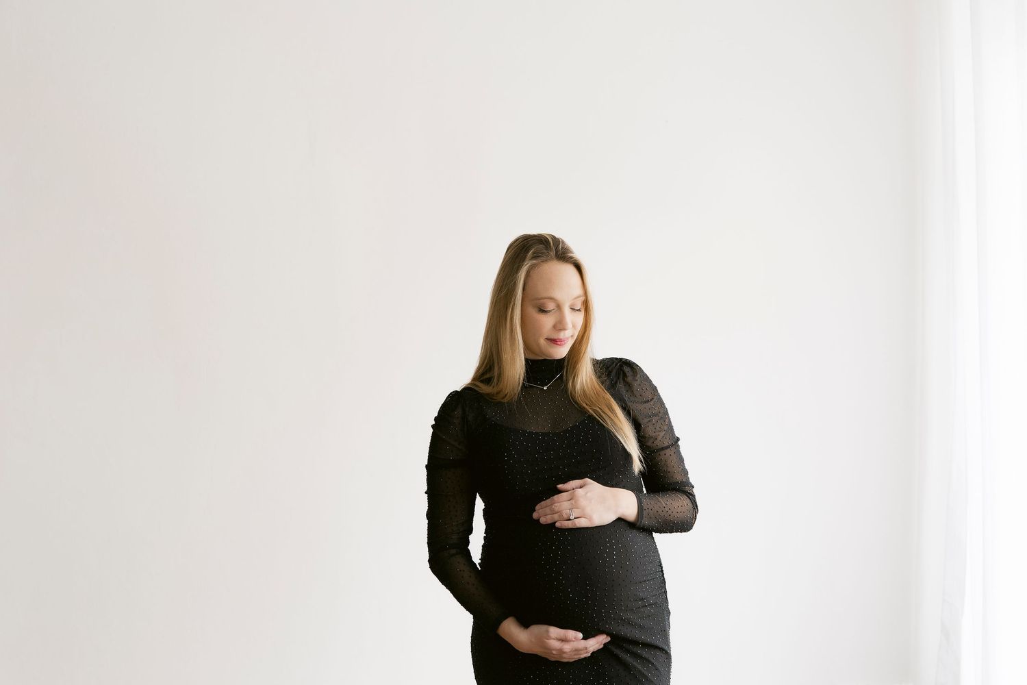 Pregnant woman in black dress cradling baby bump against white background.