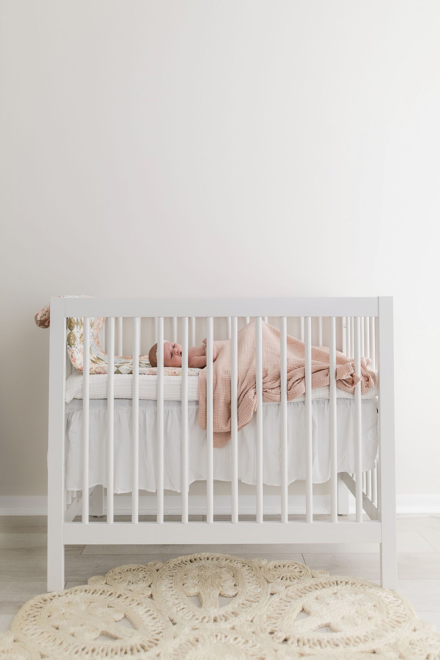 White wooden crib with soft bedding against white wall and beige textured rug.