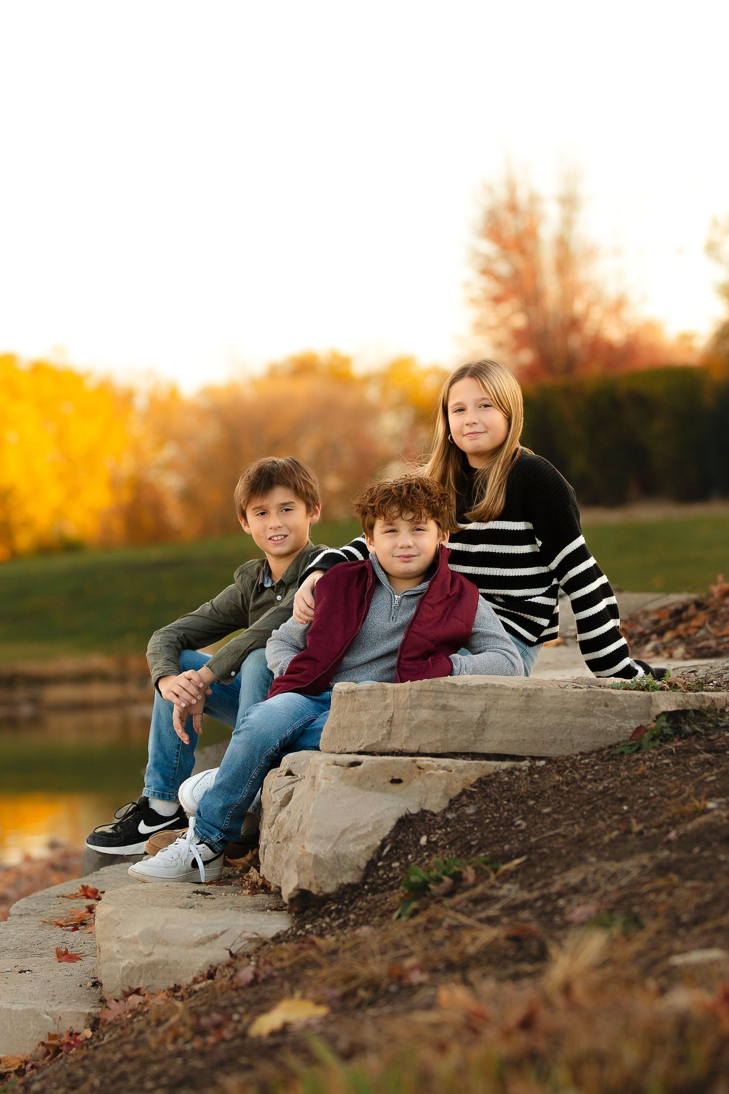 Children lay together on a rocky slope during golden hour sunset by a lake.