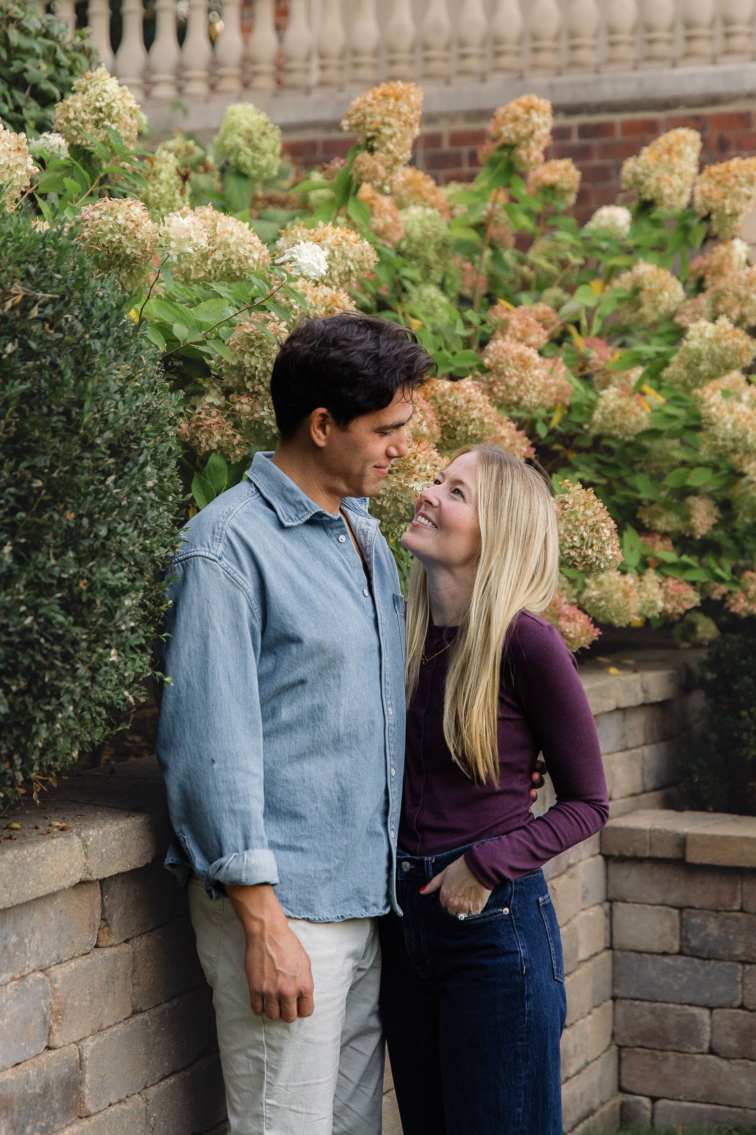 A couple shares a romantic moment against a backdrop of blooming hydrangeas and stone garden walls.