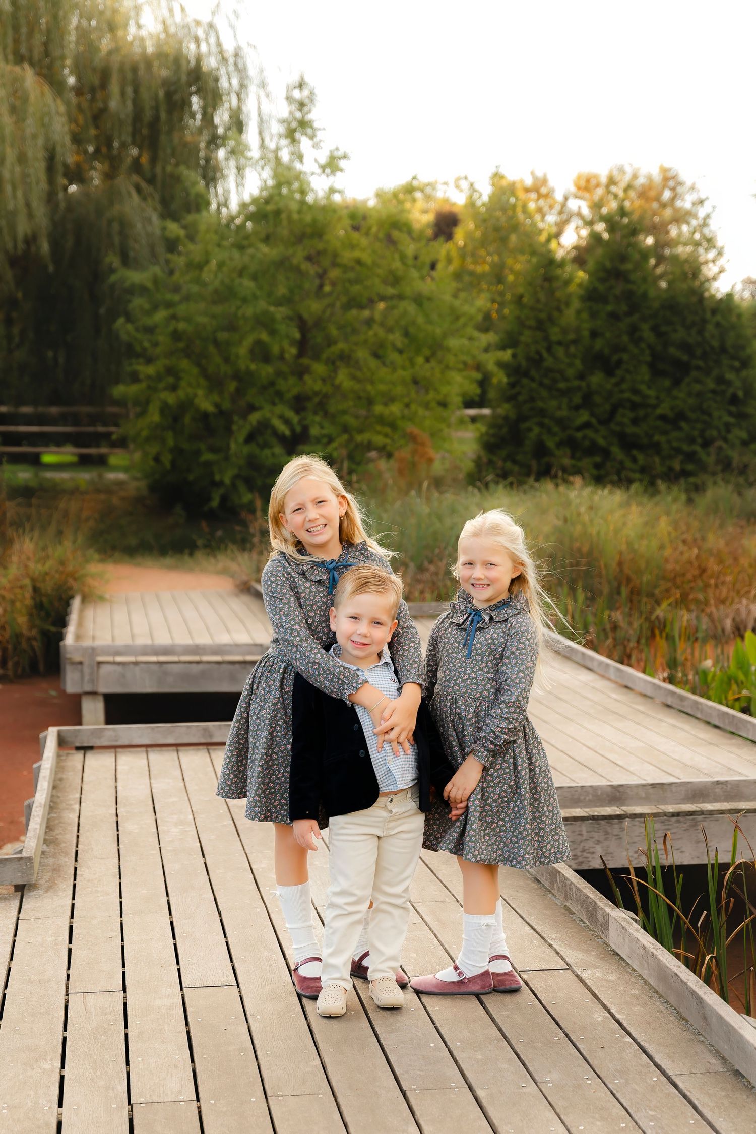 Two young children in matching outfits play and laugh together on a wooden boardwalk during golden hour.