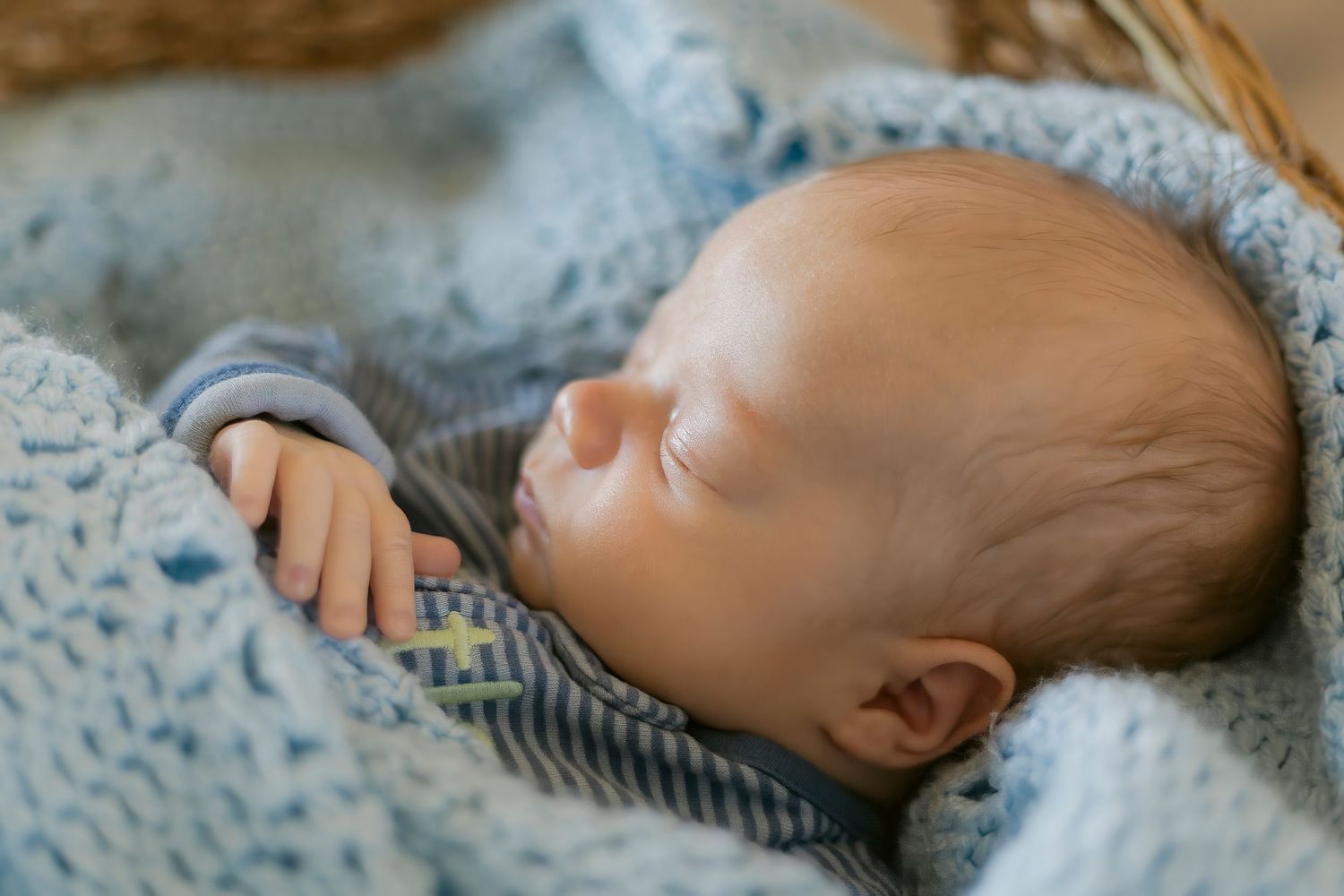 Newborn baby sleeping peacefully wrapped in a soft blue knit blanket inside a cozy wicker basket.