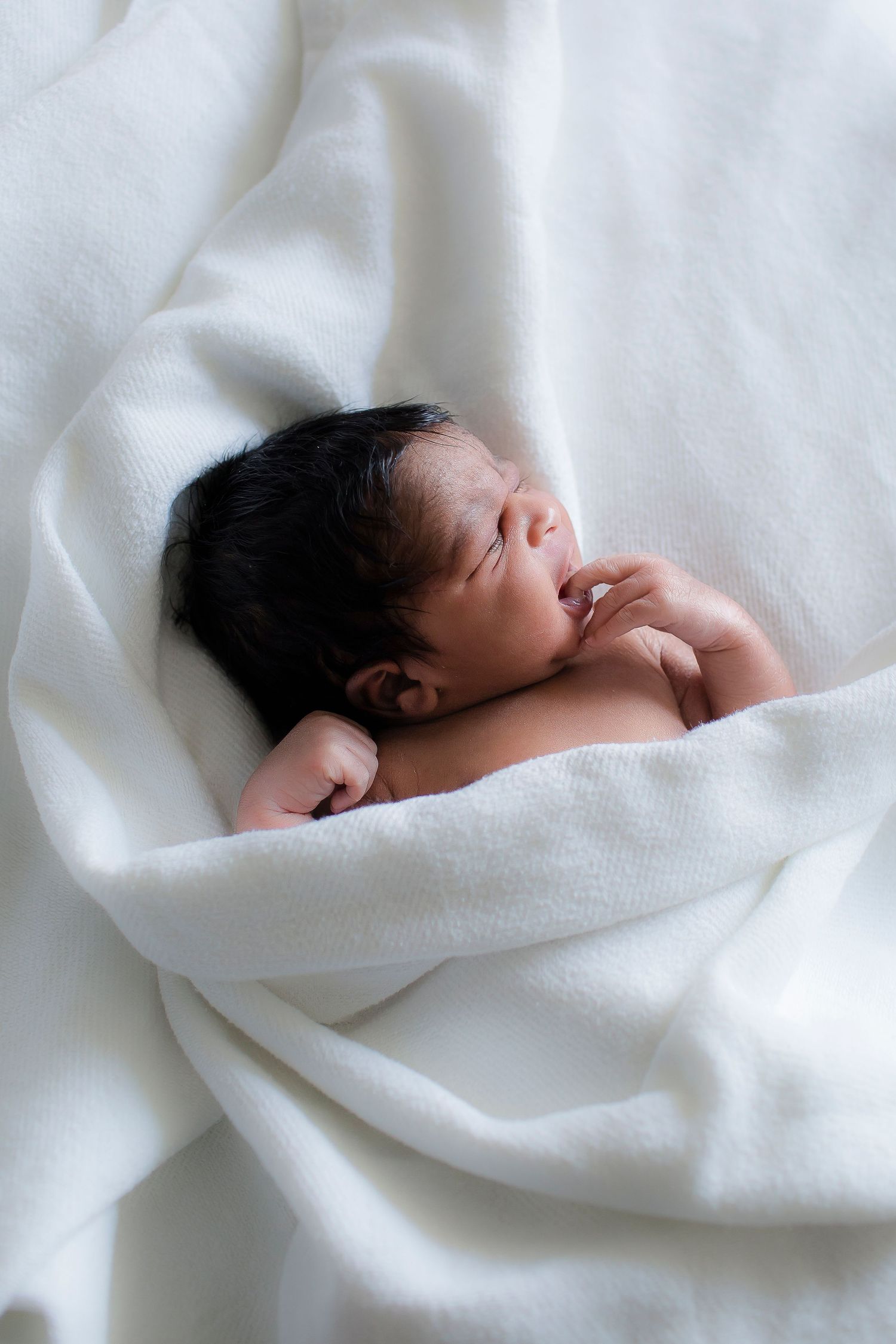 Sleeping newborn baby swaddled in soft white blanket against white background.
