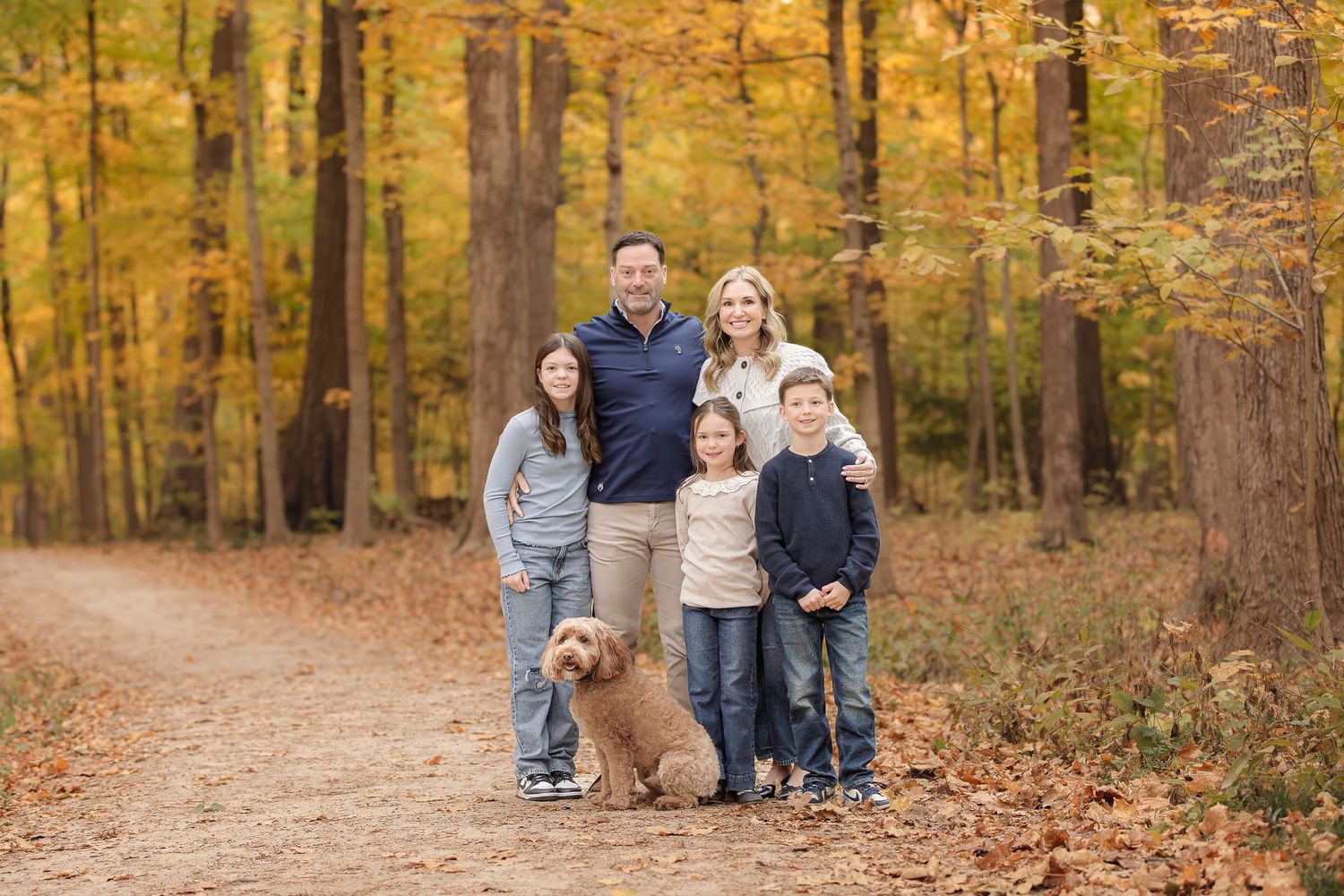 A group walks along a scenic autumn forest path covered in fallen leaves during a fall photo session.