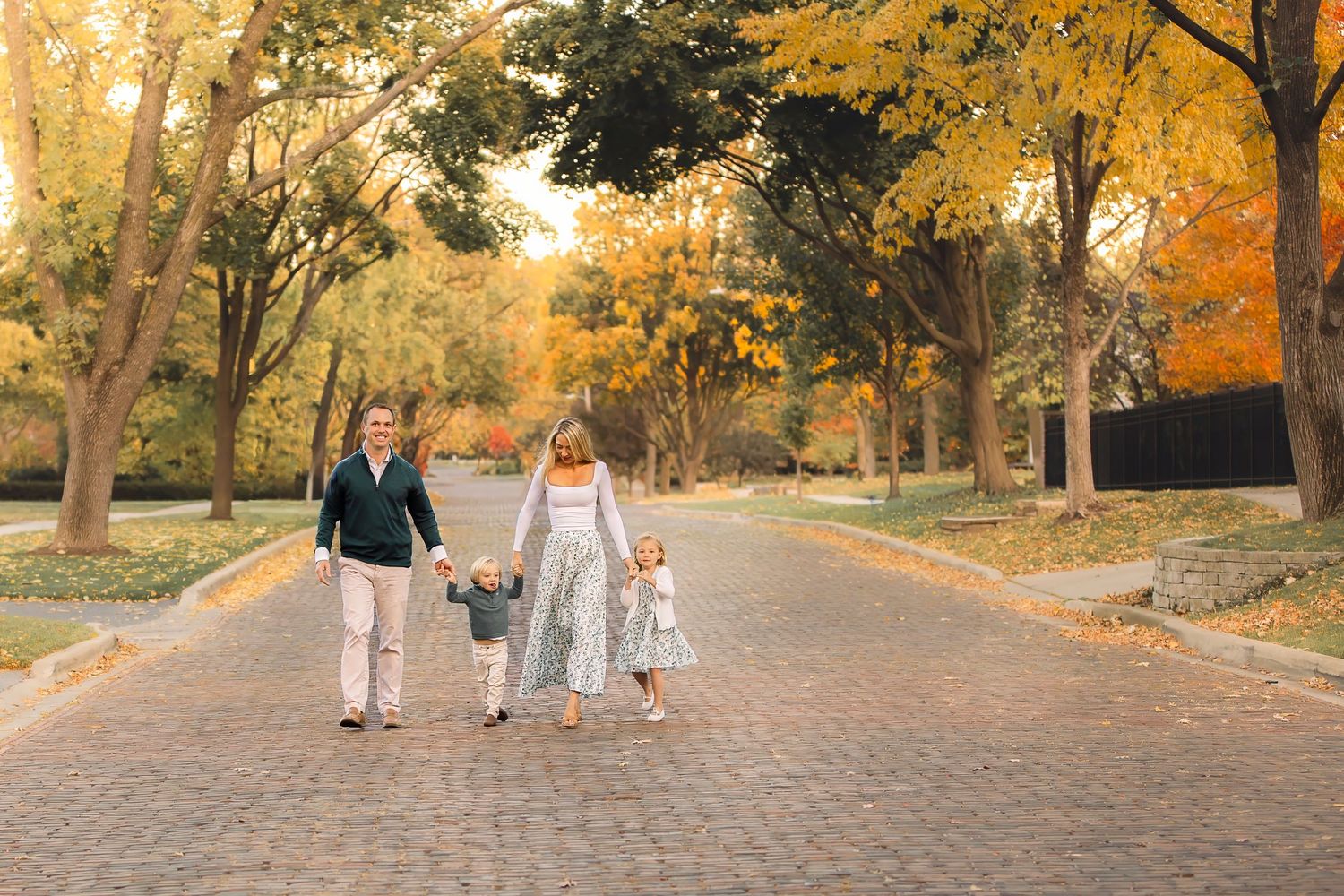 A group of people walk together on a tree-lined path during autumn with golden foliage overhead.