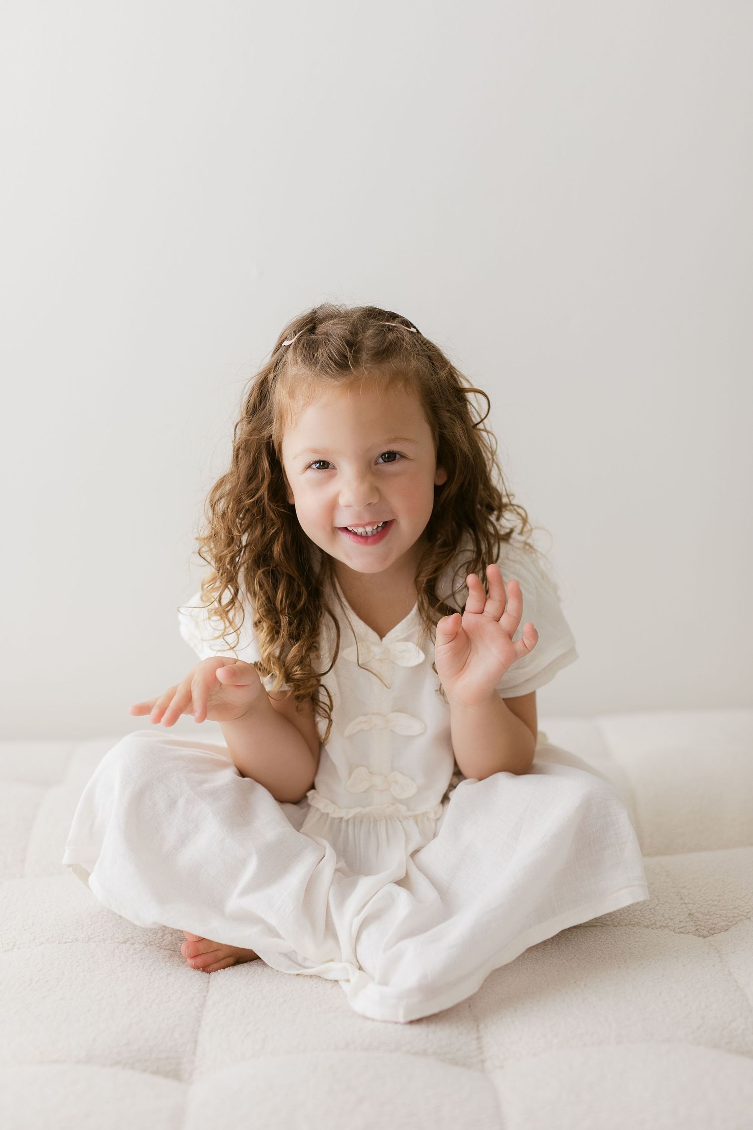 Studio portrait of young child in white dress sitting on light background.