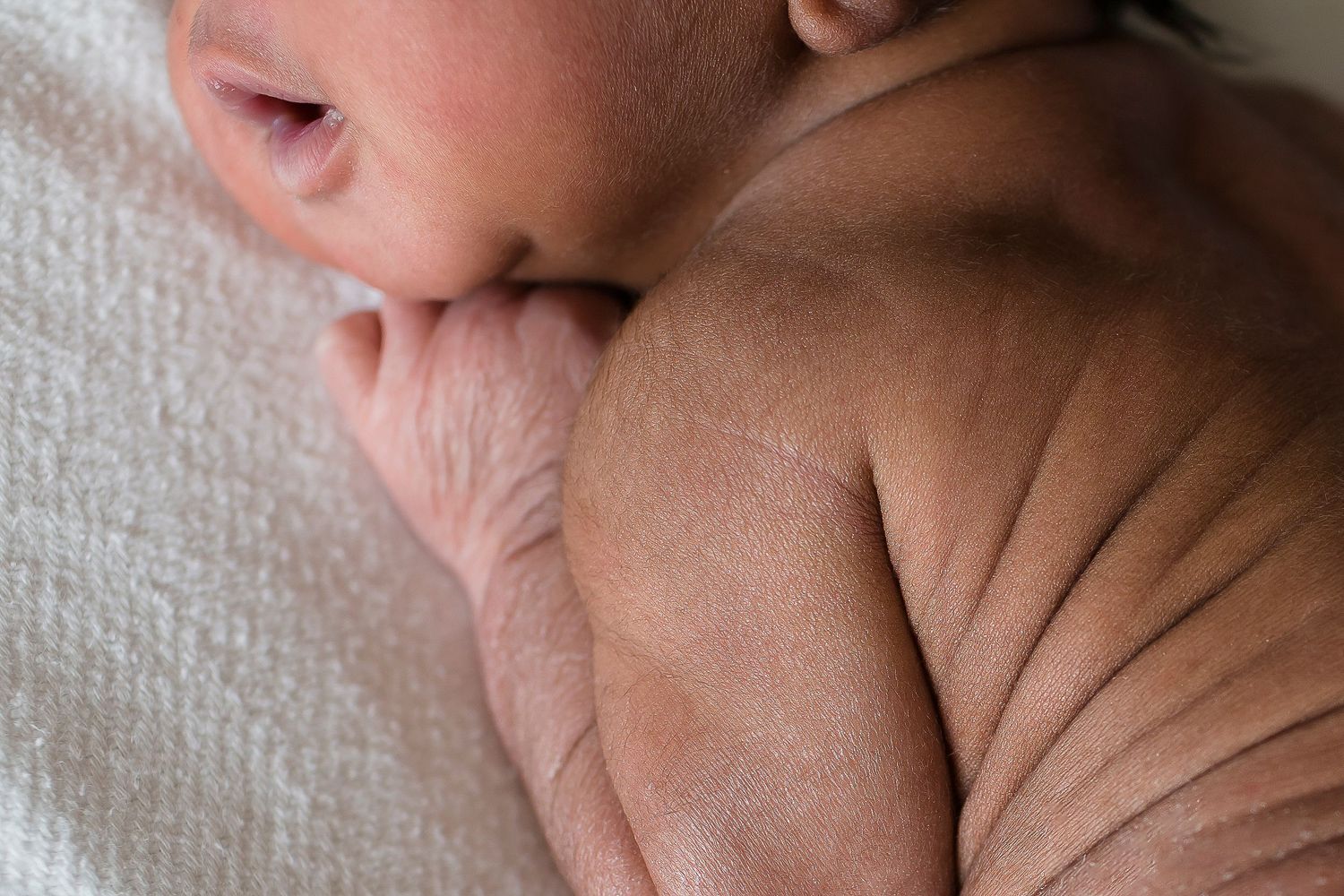 Close-up of newborn's delicate skin and tiny fingers against white fabric.