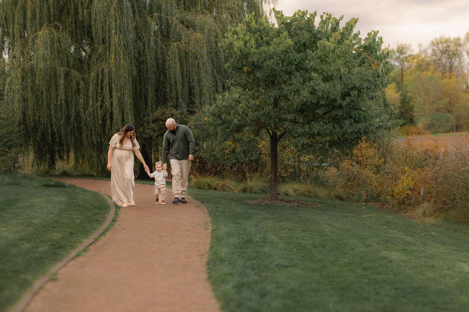 A couple walks together on a winding path through an autumn park during golden hour.