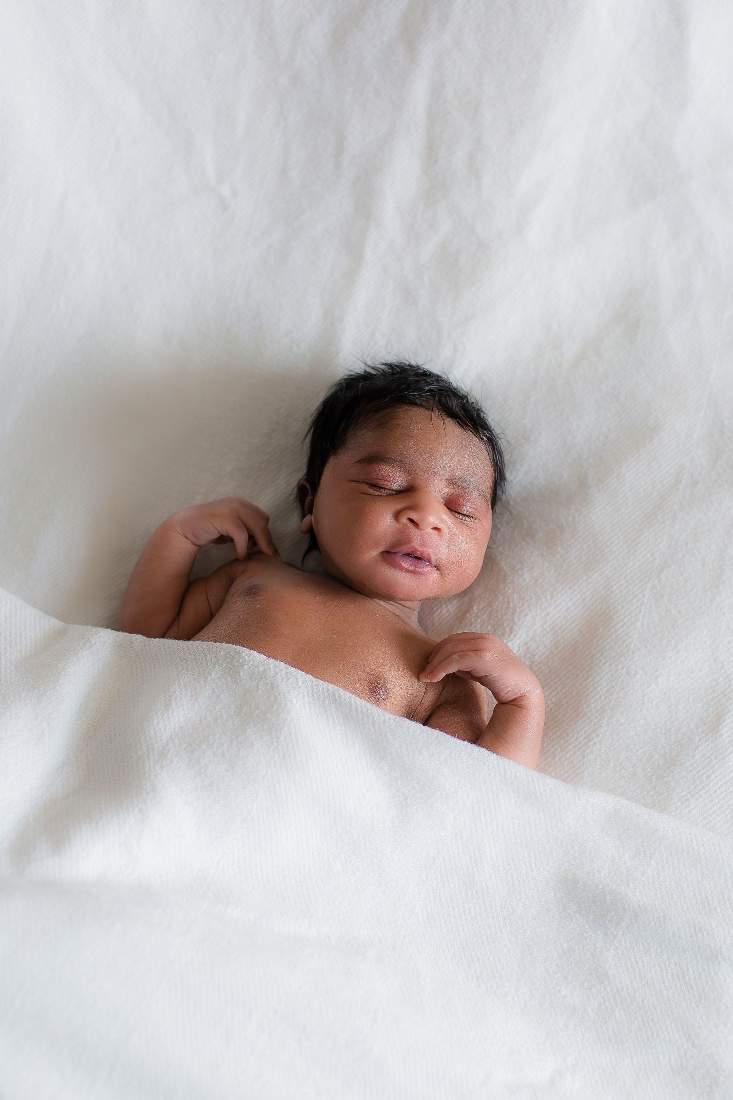 Peaceful newborn baby resting on white bedding in natural light.
