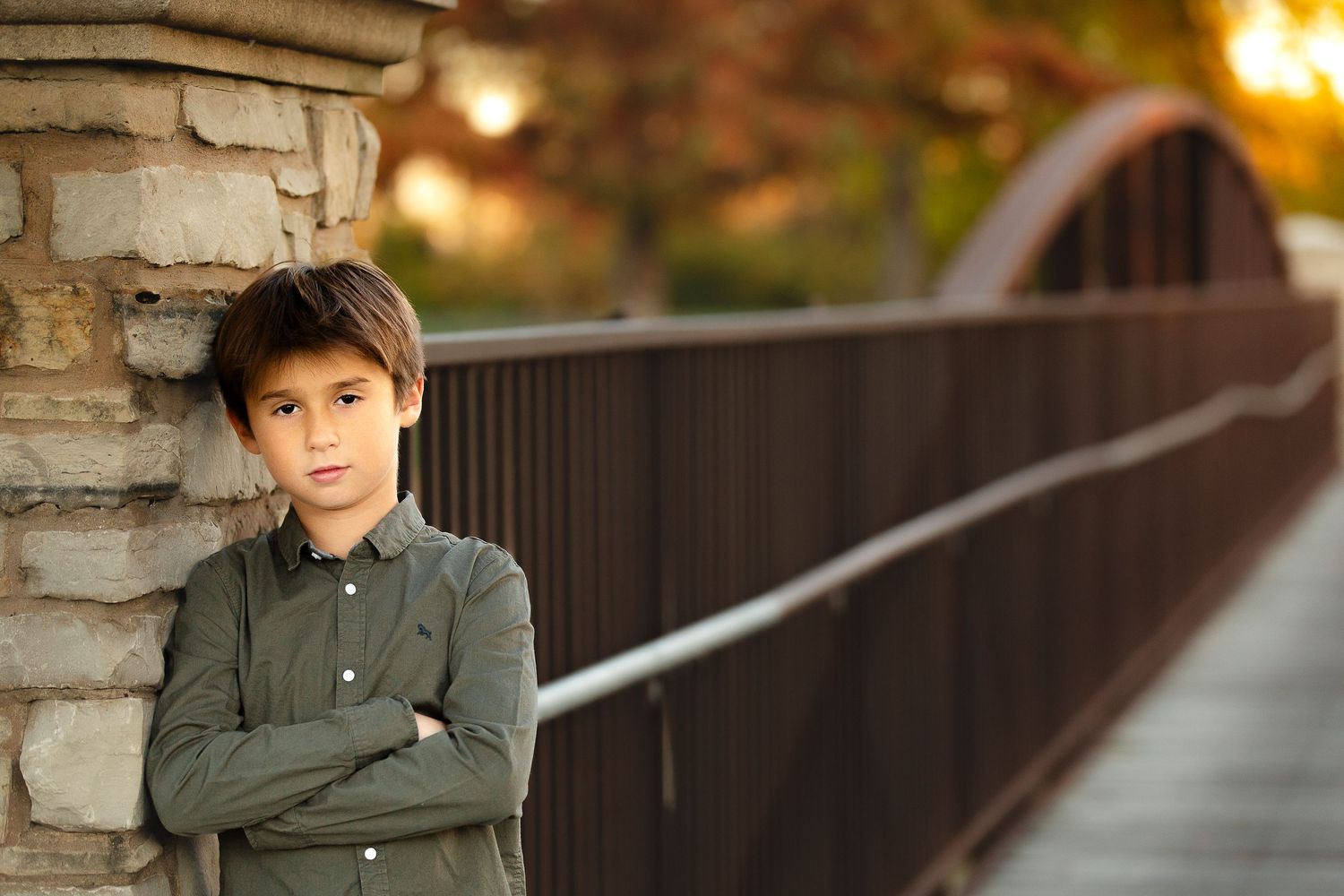 Person in olive shirt leans against stone pillar on bridge during golden hour.