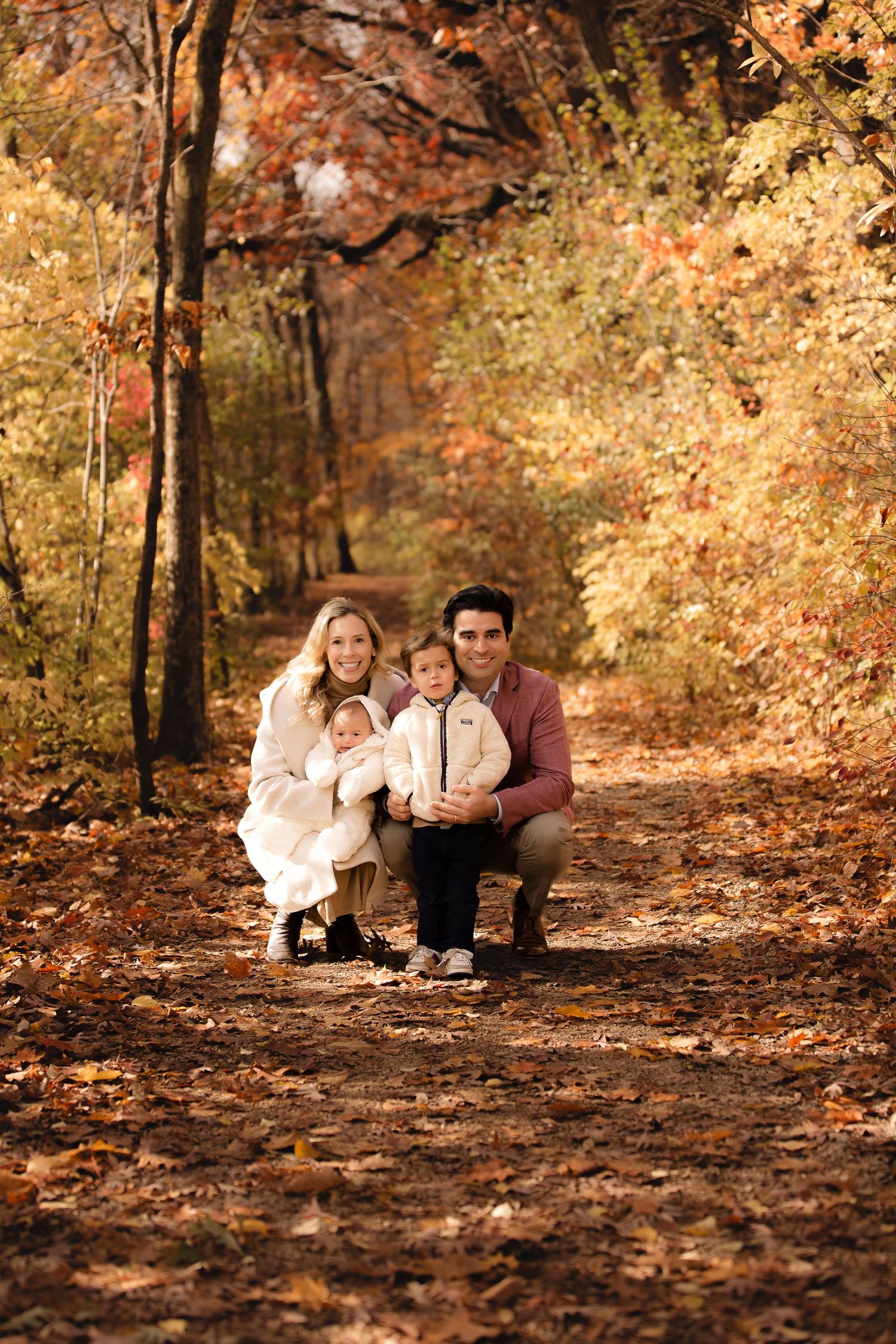 A group sits together on fallen autumn leaves in a wooded area with golden foliage in the background.