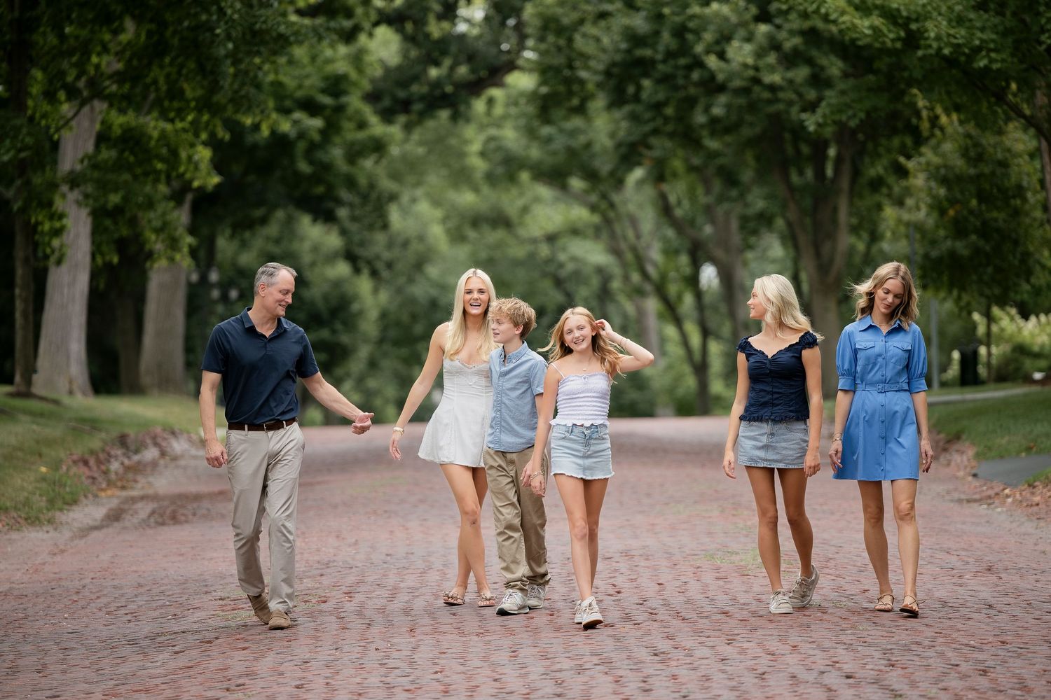 Family of six walking together on a tree-lined brick path outdoors.