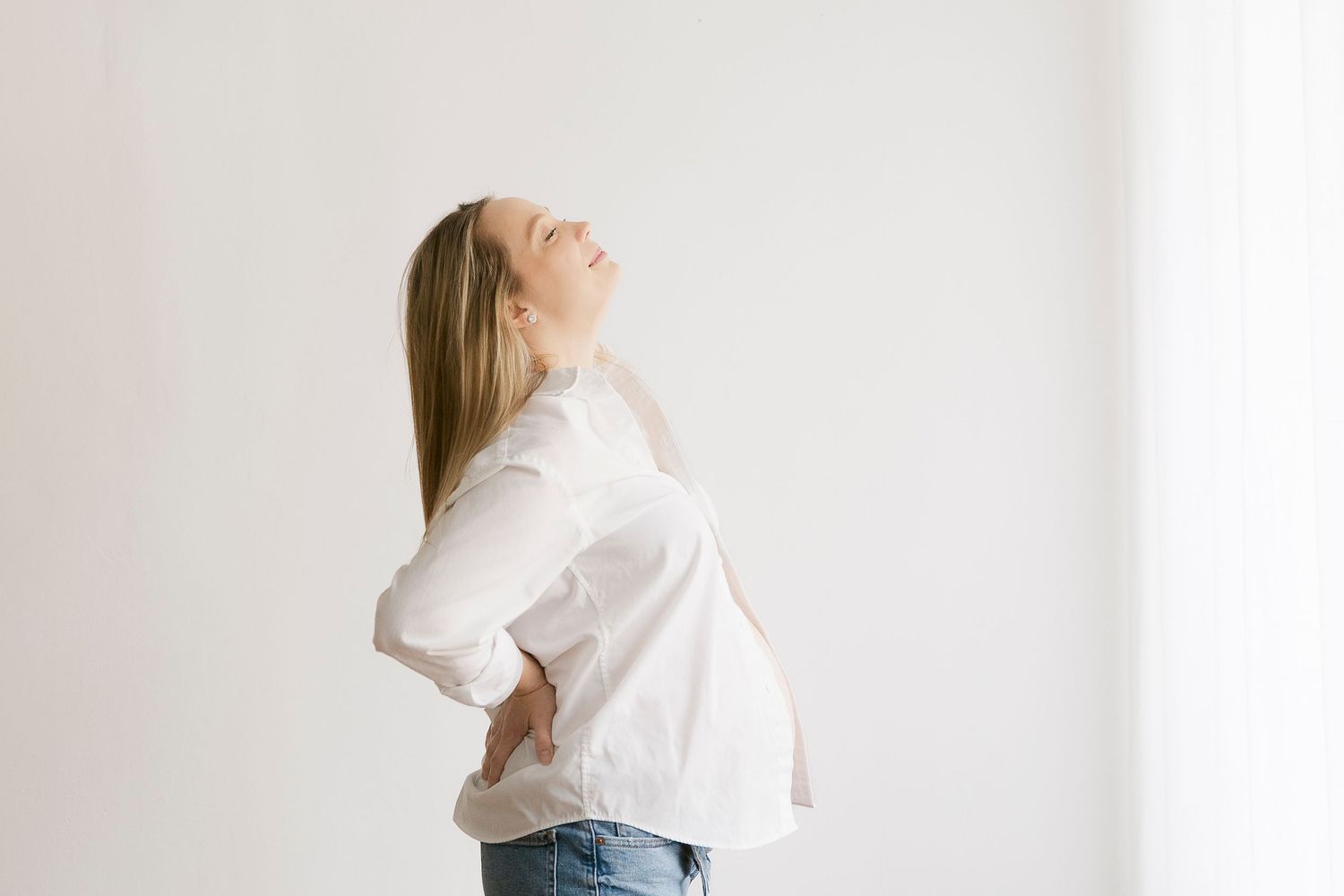 Person in white shirt and jeans stands against light background in minimalist fashion photography series.
