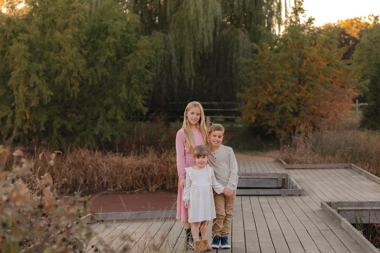 A family poses together on a wooden deck during golden hour in an autumn setting with fall foliage in the background.