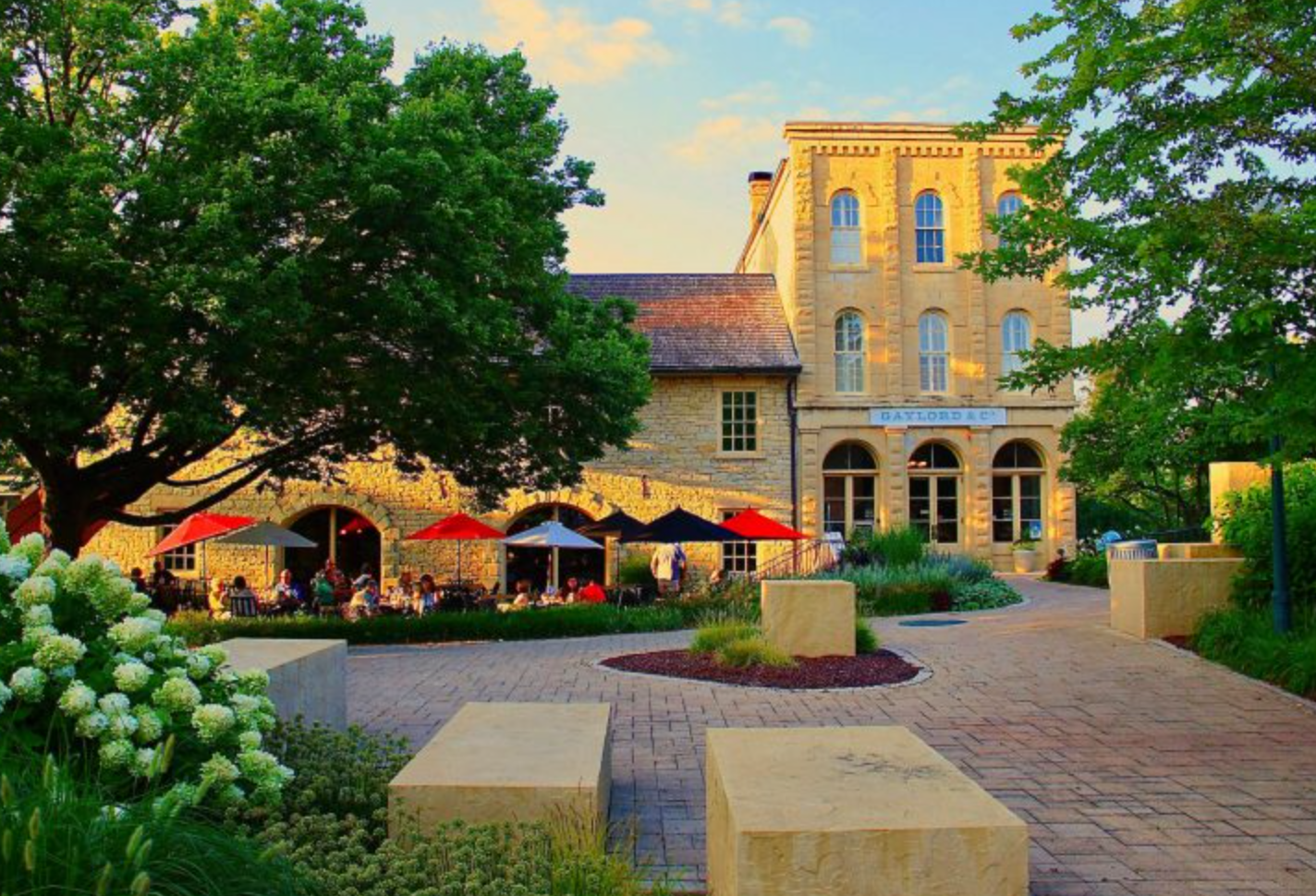 Charming stone building with outdoor patio, colorful umbrellas, and lush gardens at golden hour.