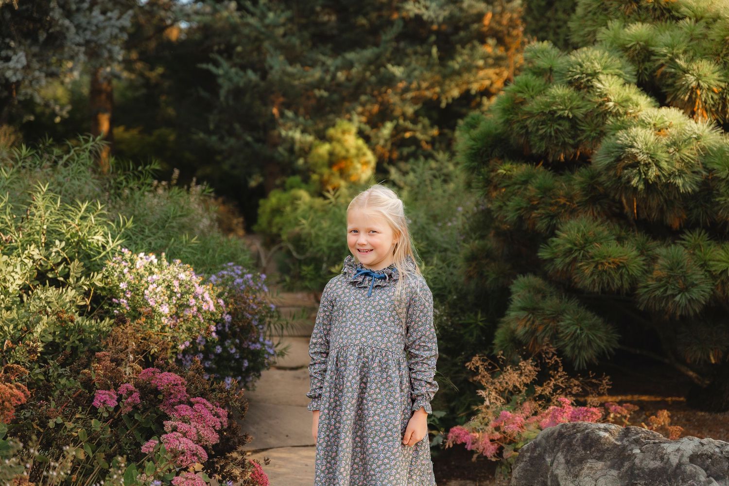 A garden path winds through vibrant fall foliage and blooming azaleas in a peaceful woodland setting.