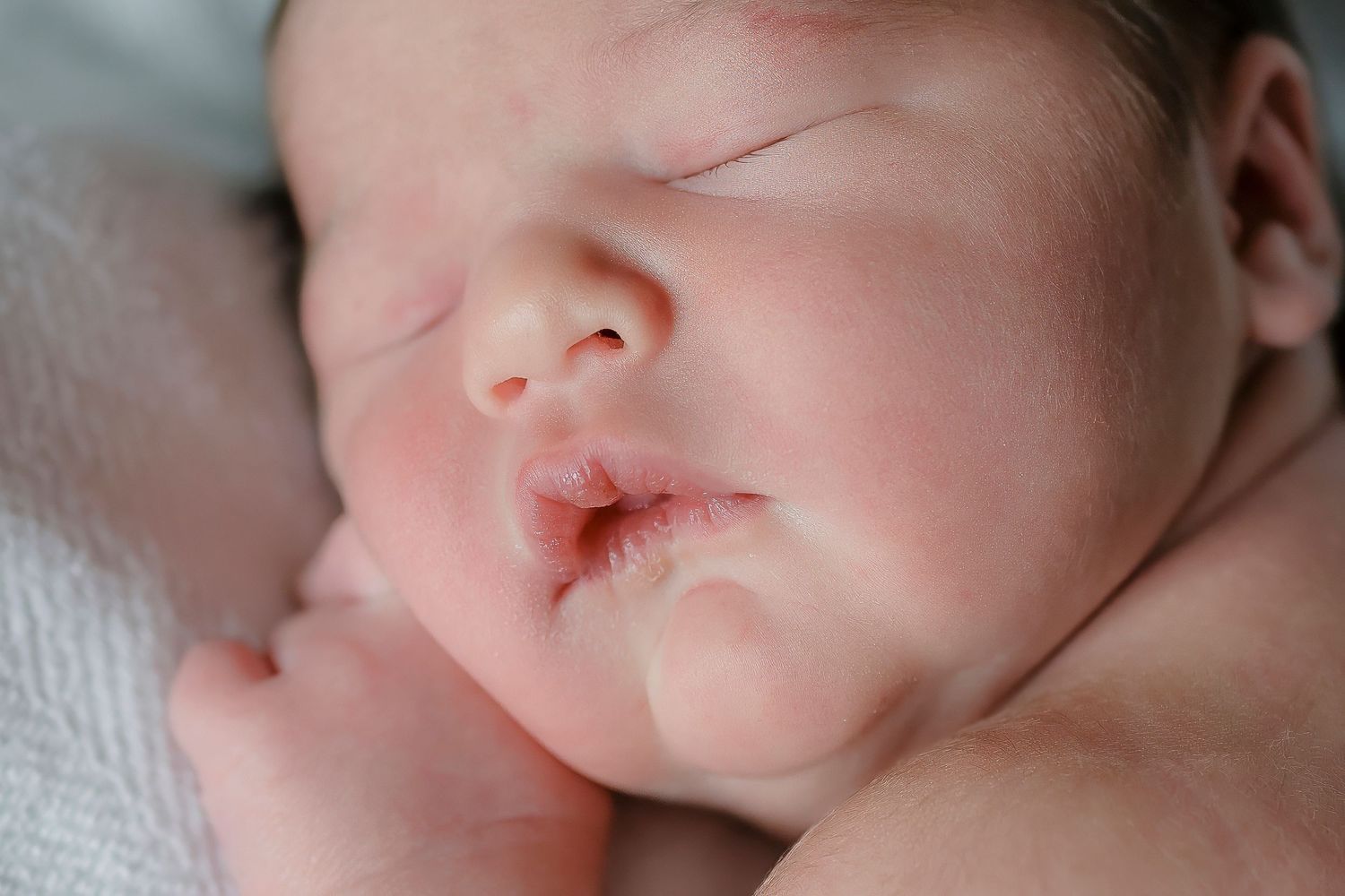 Peaceful sleeping newborn with soft features resting on white bedding.