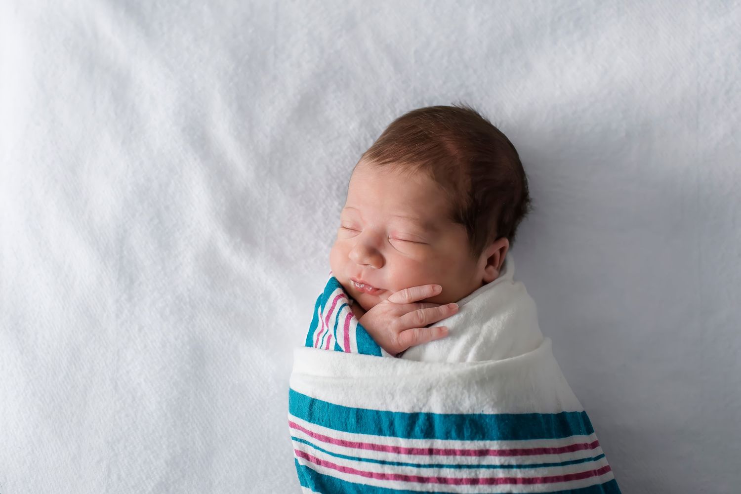 Newborn baby swaddled in white and turquoise blanket resting on white background in multiple poses.