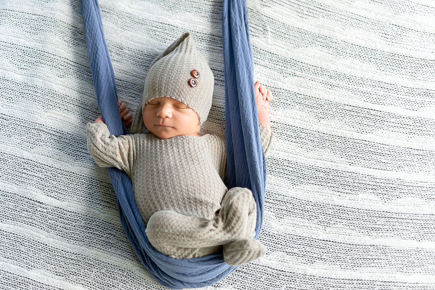 A gray and white cat sleeps peacefully in a cozy blue hammock bed mounted on a wall.