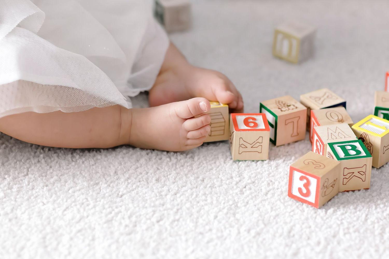 Wooden alphabet blocks arranged on a soft white carpet with small feet visible in the background.
