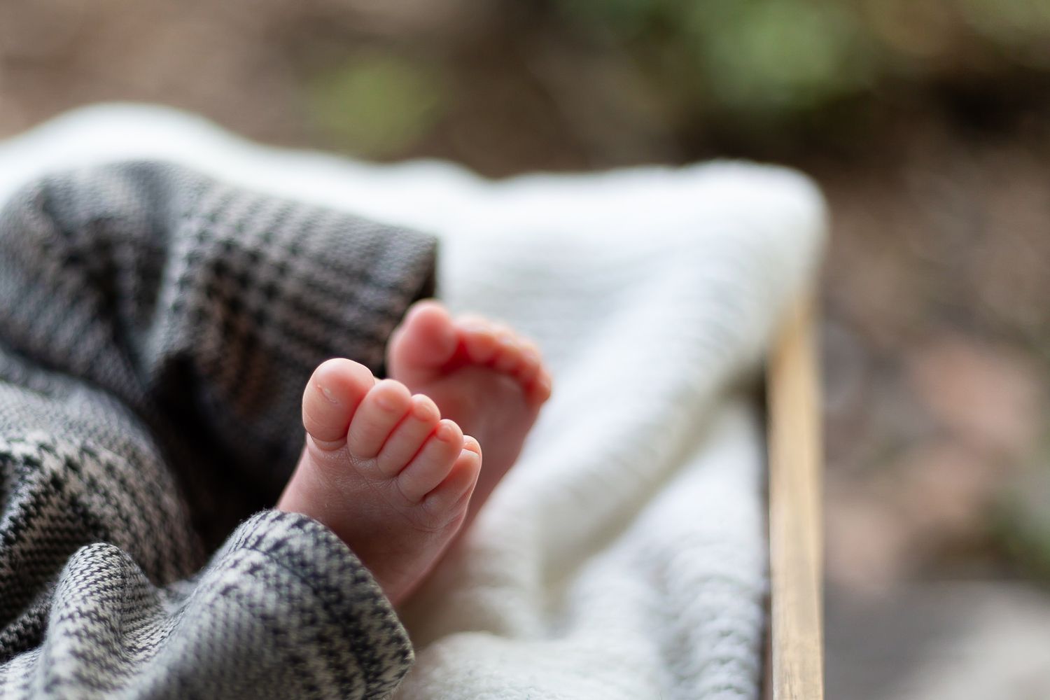 Close-up of tiny baby foot resting on gray and white knitted fabric.
