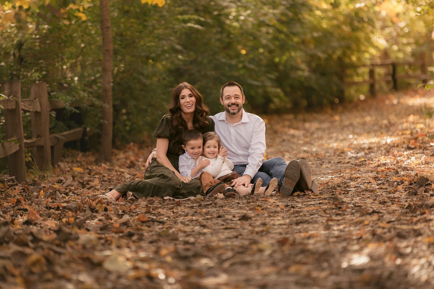 People enjoying a fall day sitting among fallen leaves in a sunlit wooded area.