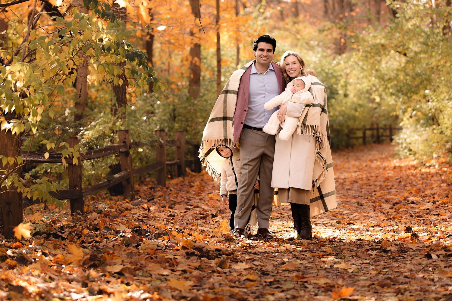 A family plays together in a scenic autumn forest with fallen orange leaves covering the ground.