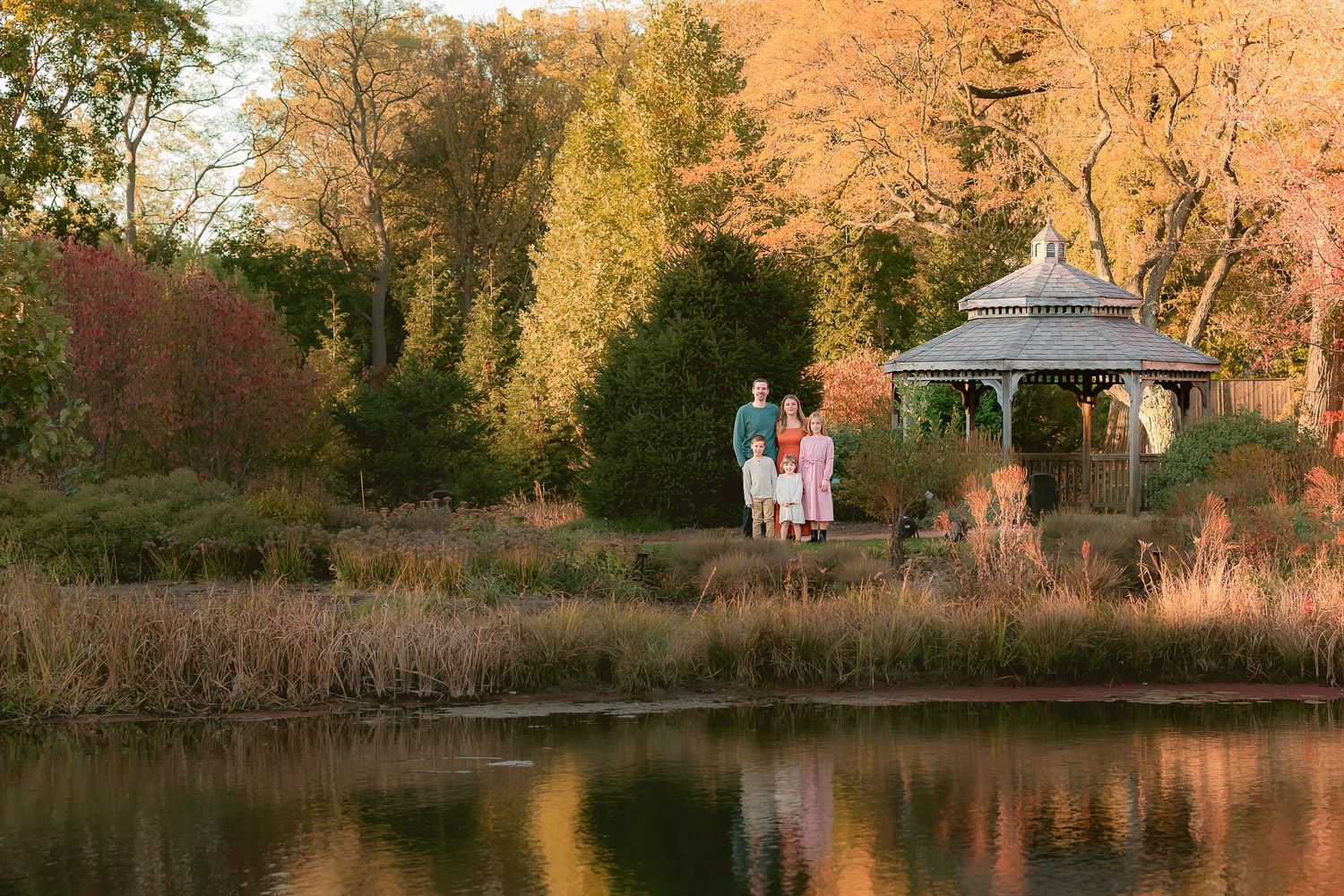 Scenic autumn landscape with a gazebo by a pond reflecting warm sunset colors.