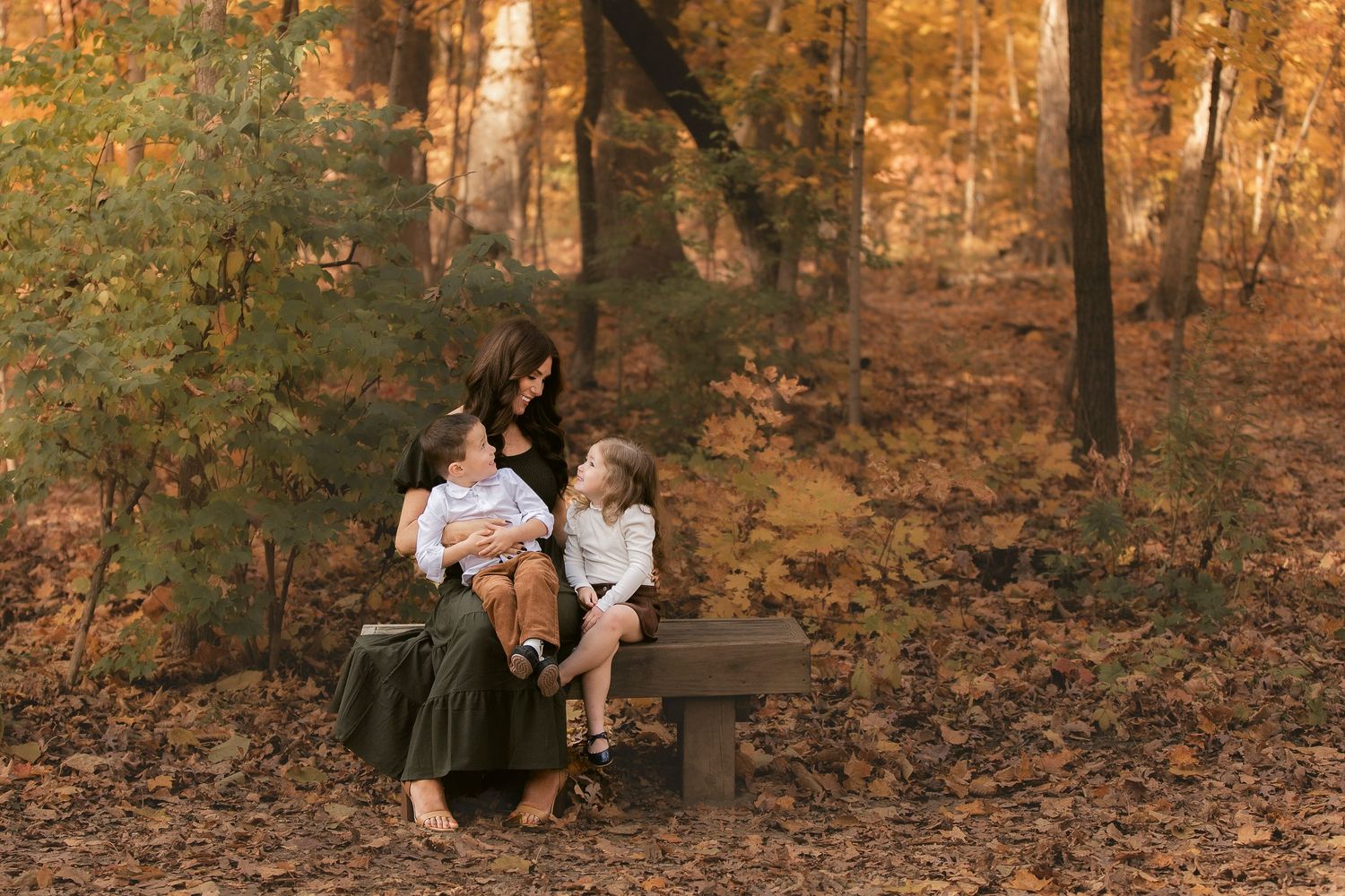 Couple sitting together on wooden bench surrounded by autumn foliage in a peaceful forest setting.