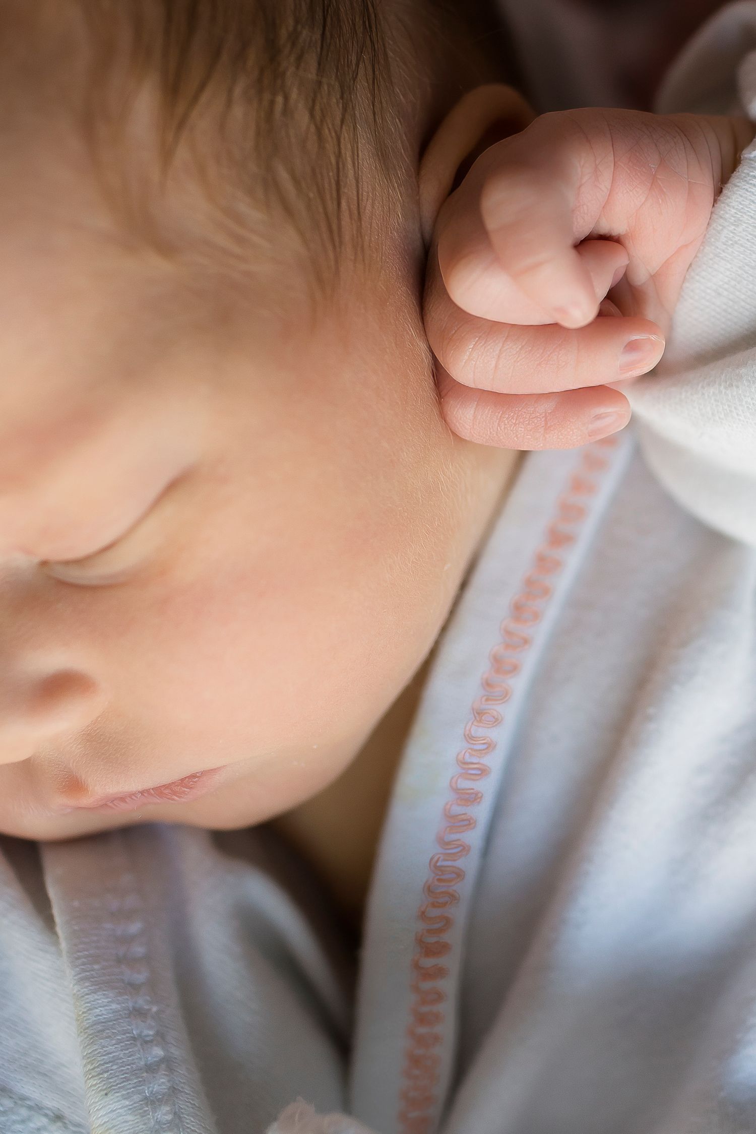 A sleeping baby's face in close-up with tiny fist curled near their cheek.