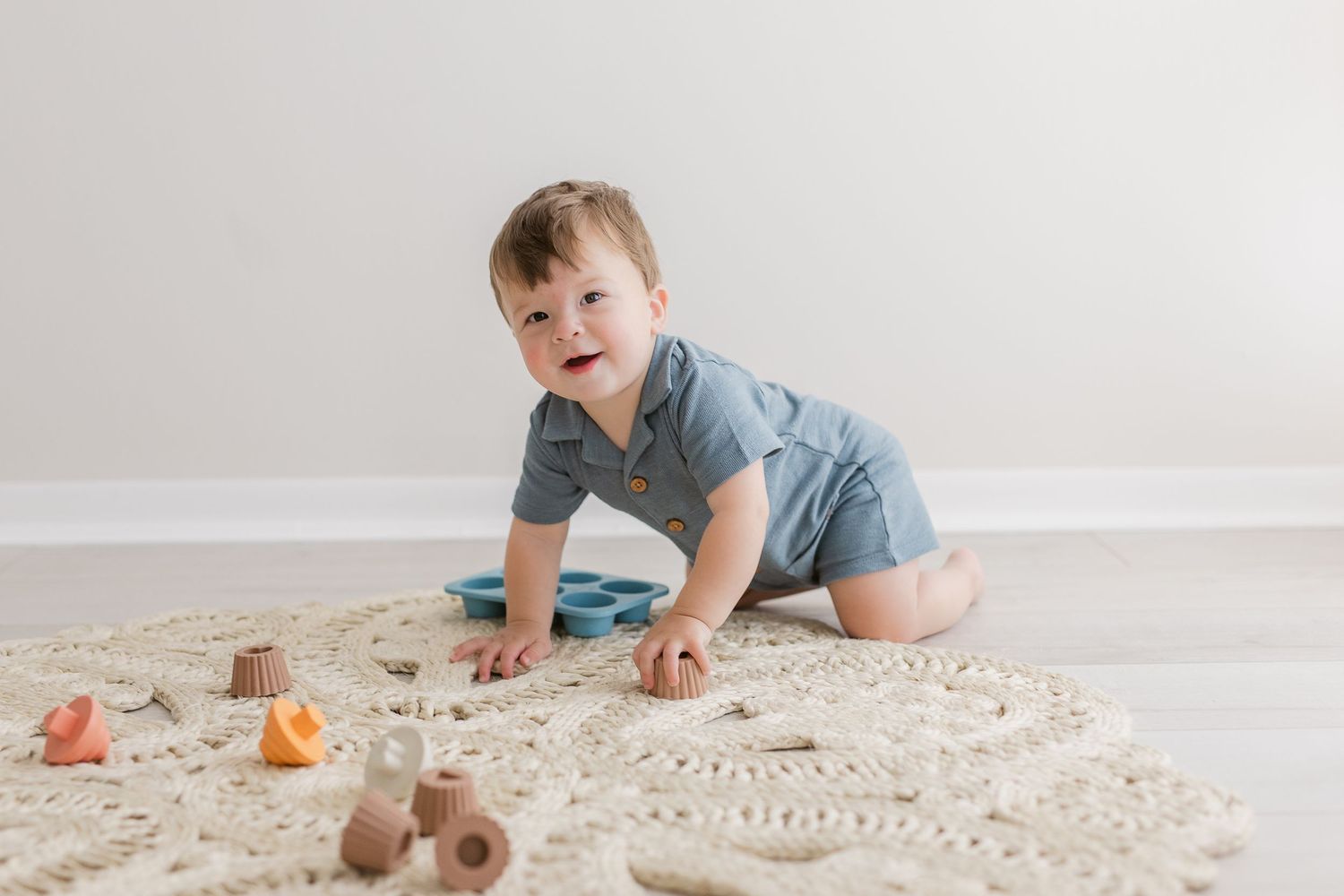 Toddler crawling on decorative rug with wooden toys in bright room.