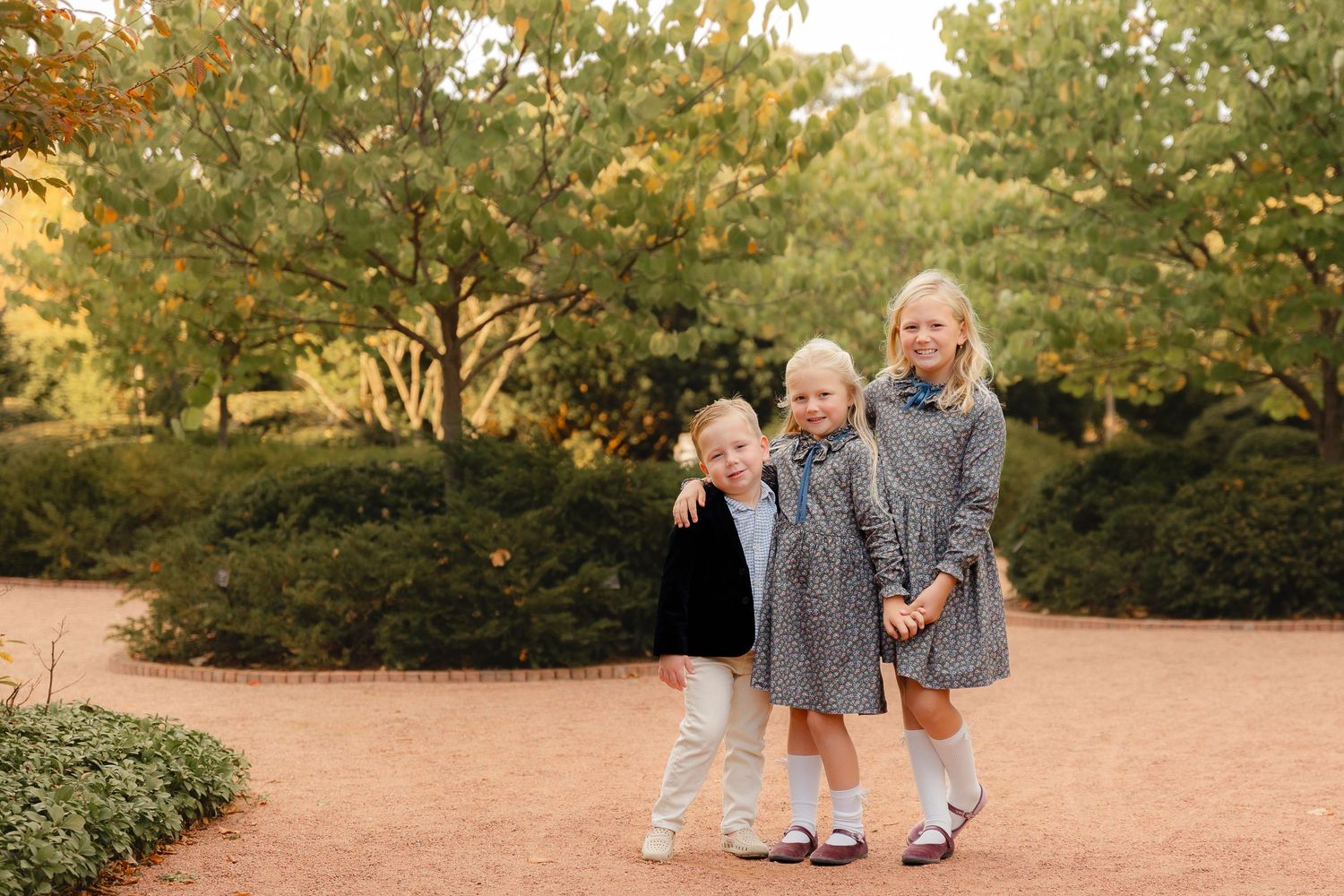 A family wearing coordinated gray outfits walks together on a dirt path during golden hour in a park setting.