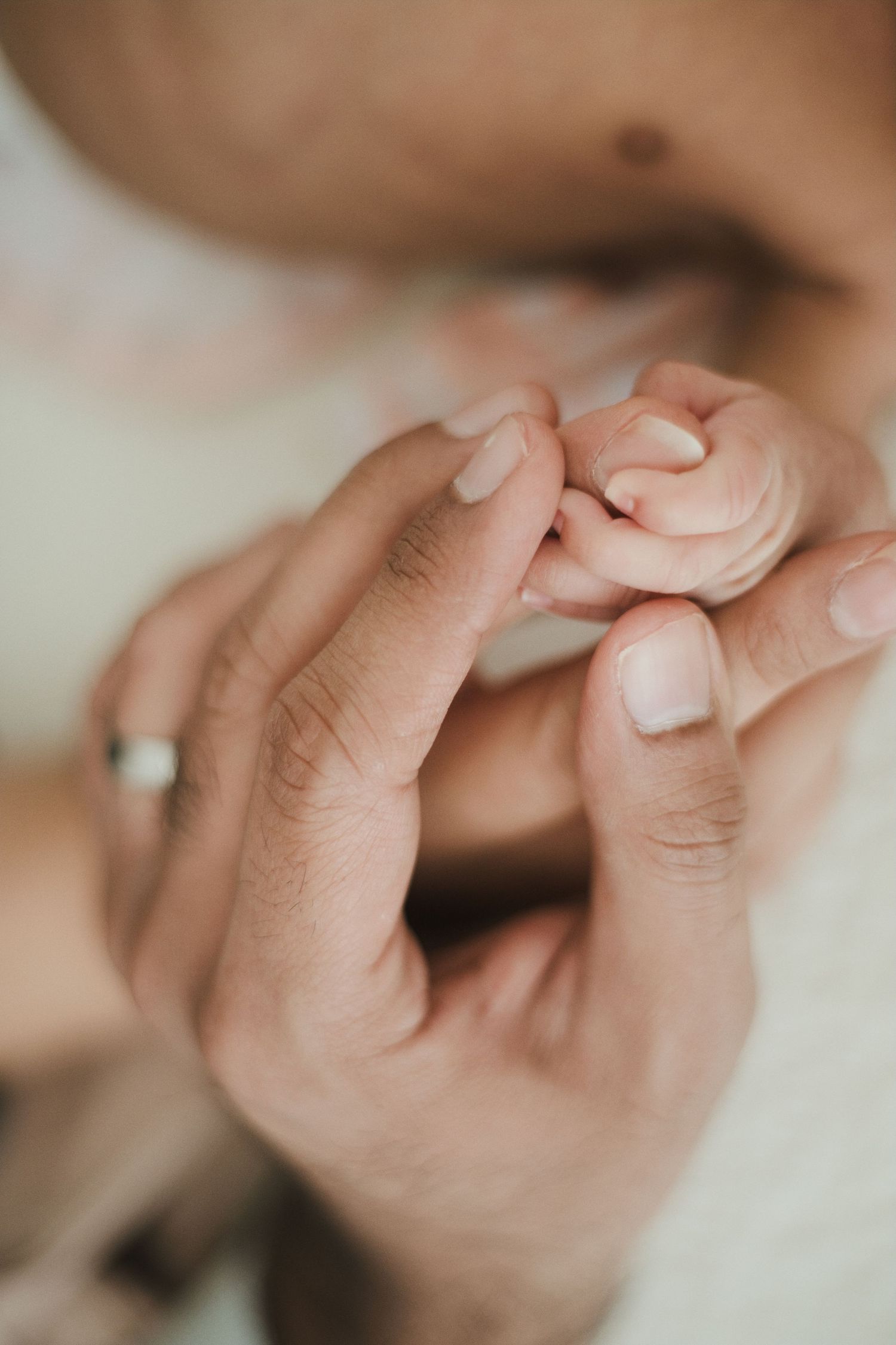 A newborn baby grasping an adult's finger, symbolizing the tender bond between parent and child.