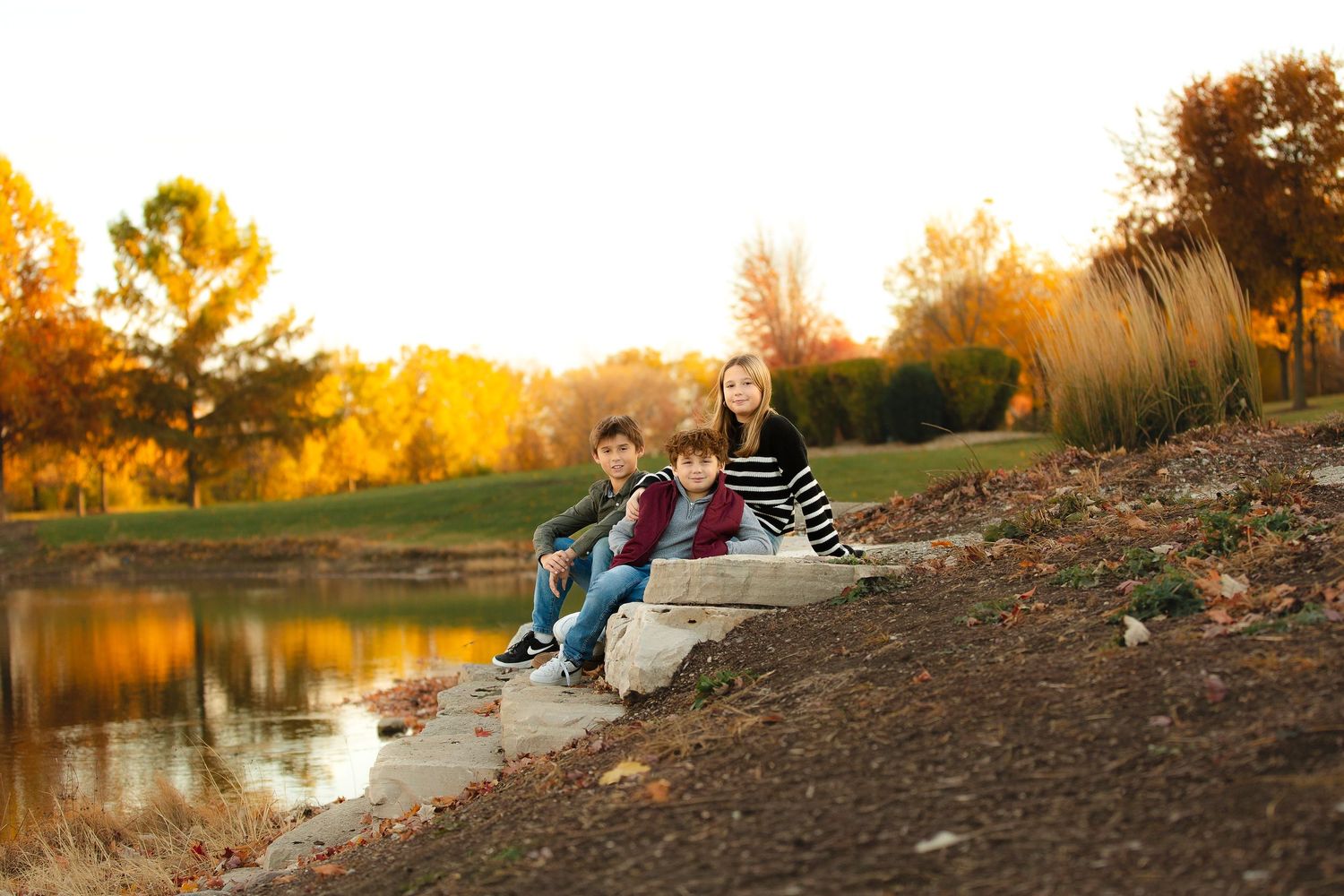 A group sits on a rocky riverbank at sunset creating a peaceful outdoor scene in golden light.