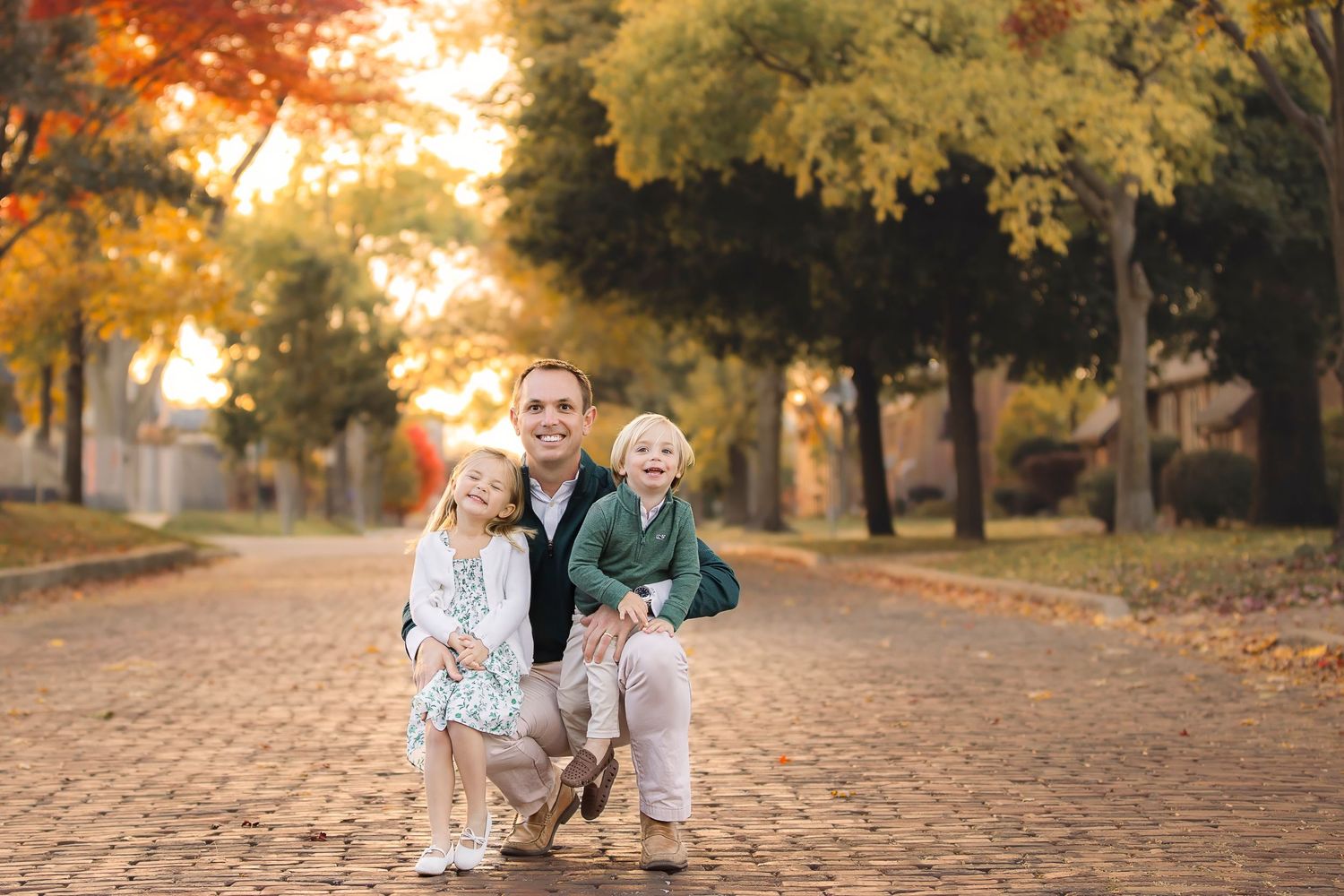 A scenic autumn scene on a brick path with golden trees and fallen leaves during sunset.