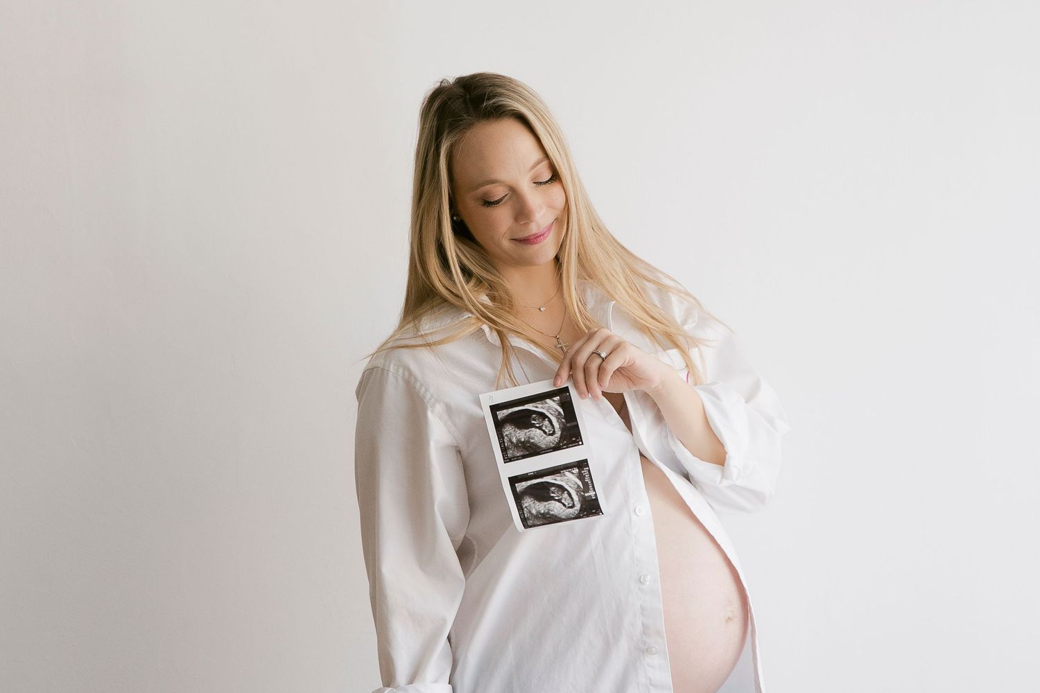 Pregnancy announcement photo collage showing ultrasound image and person in white dress touching their stomach.