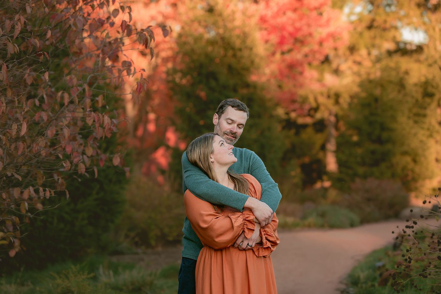 A couple embraces in a romantic autumn setting with golden sunlight filtering through colorful fall foliage.