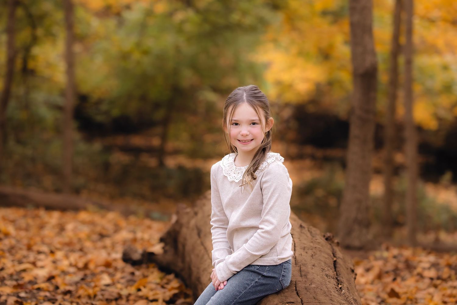 A person sits on fallen autumn leaves in a forest surrounded by vibrant orange and yellow foliage.