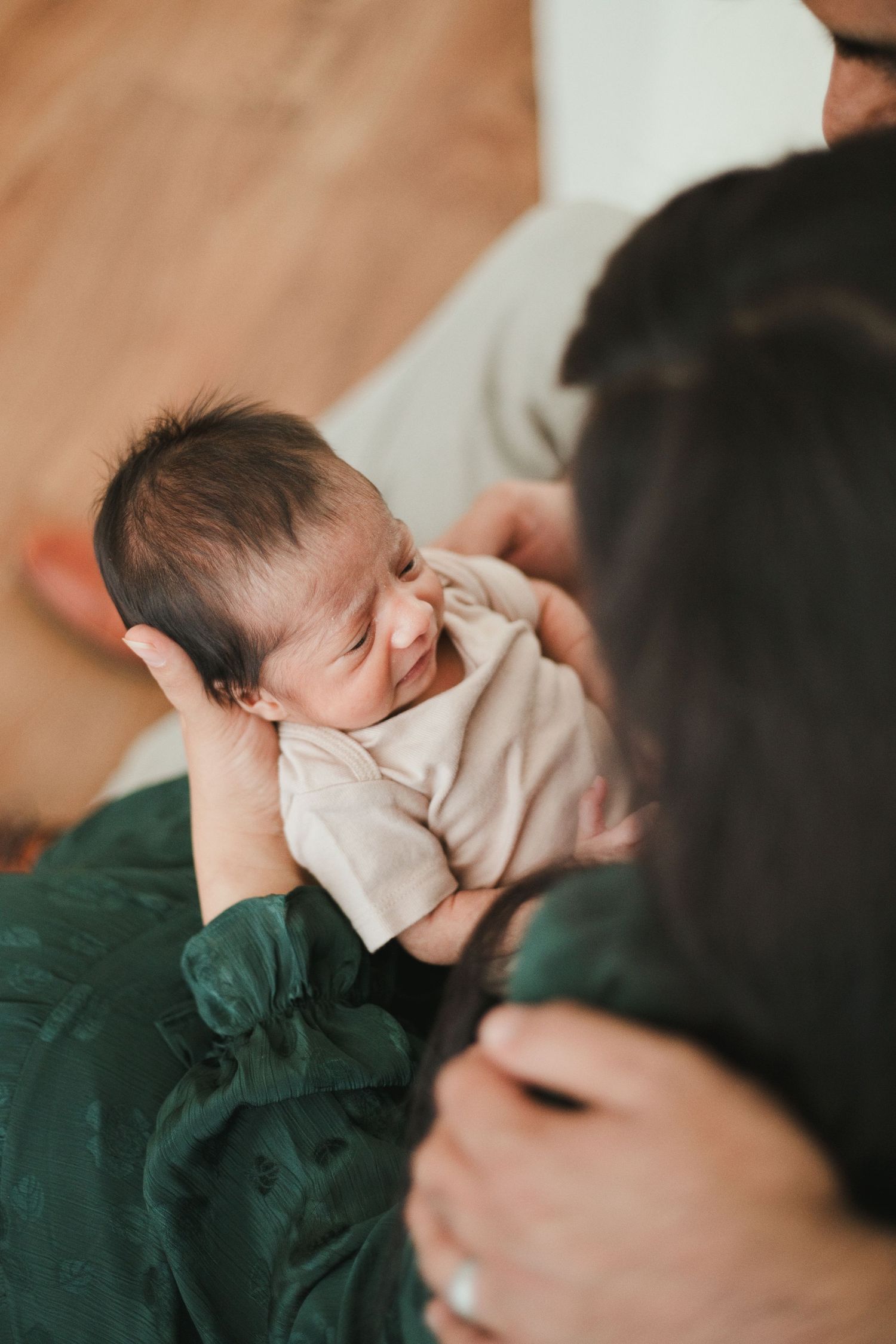 Parents lovingly holding their newborn baby, with mother in green dress cradling the infant indoors.