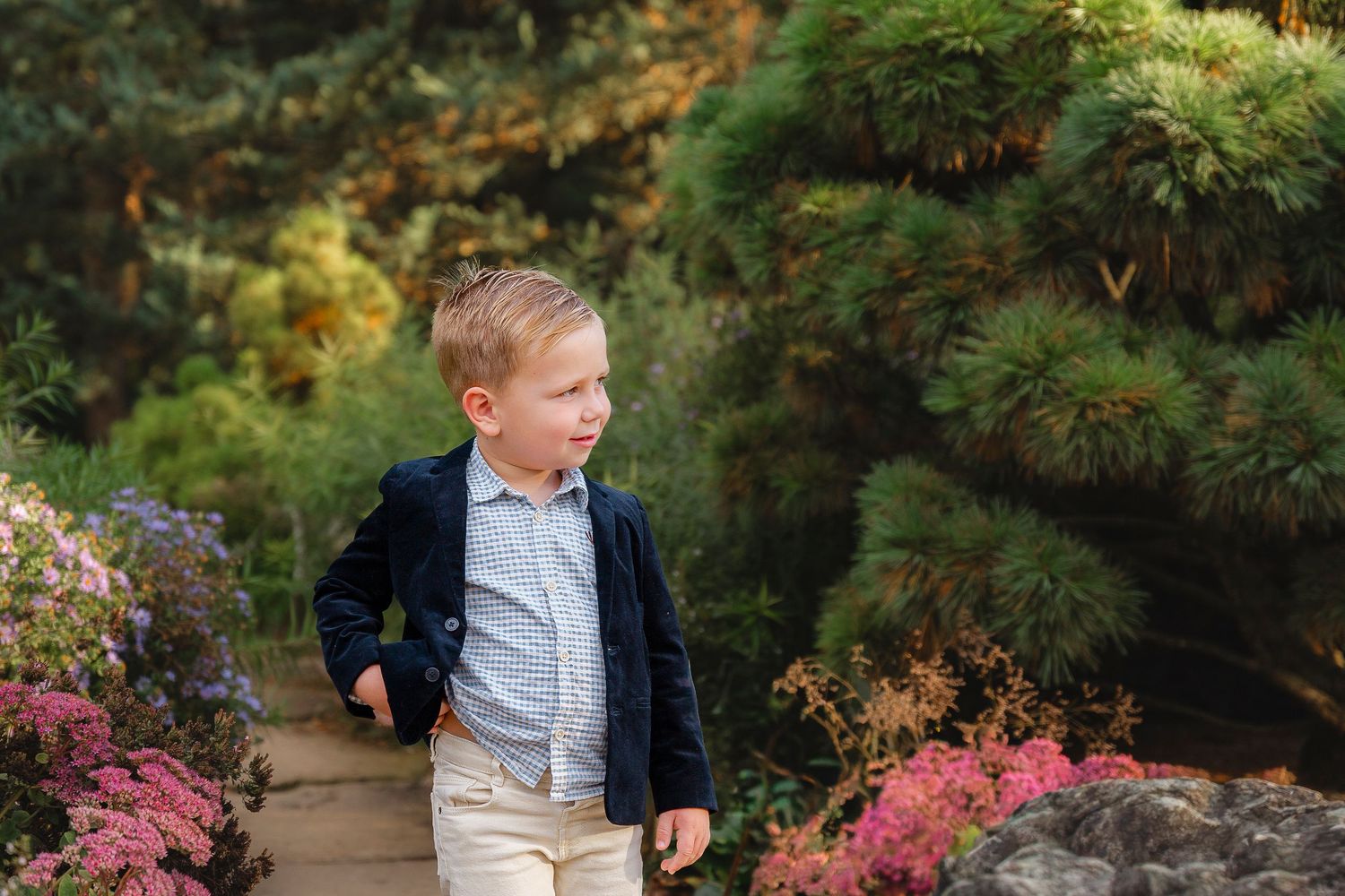 A child walks along a garden path surrounded by vibrant pink azalea bushes and lush greenery on a sunny day.