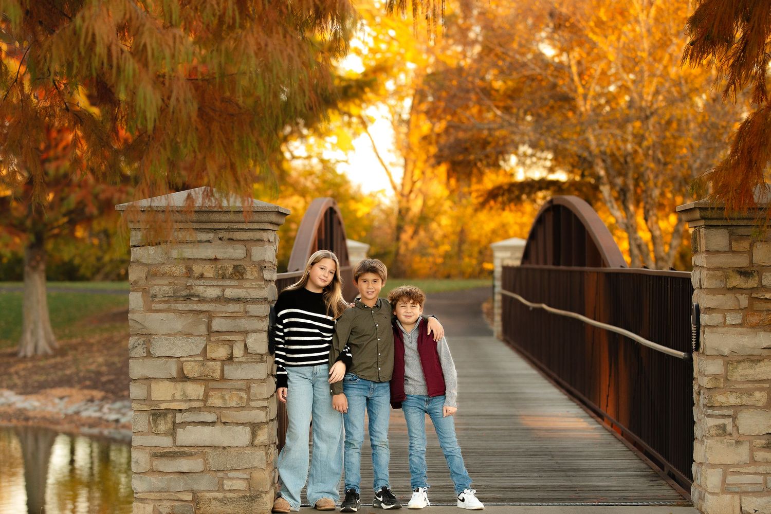 Family poses together on rustic stone bridge during golden autumn sunset in park setting.