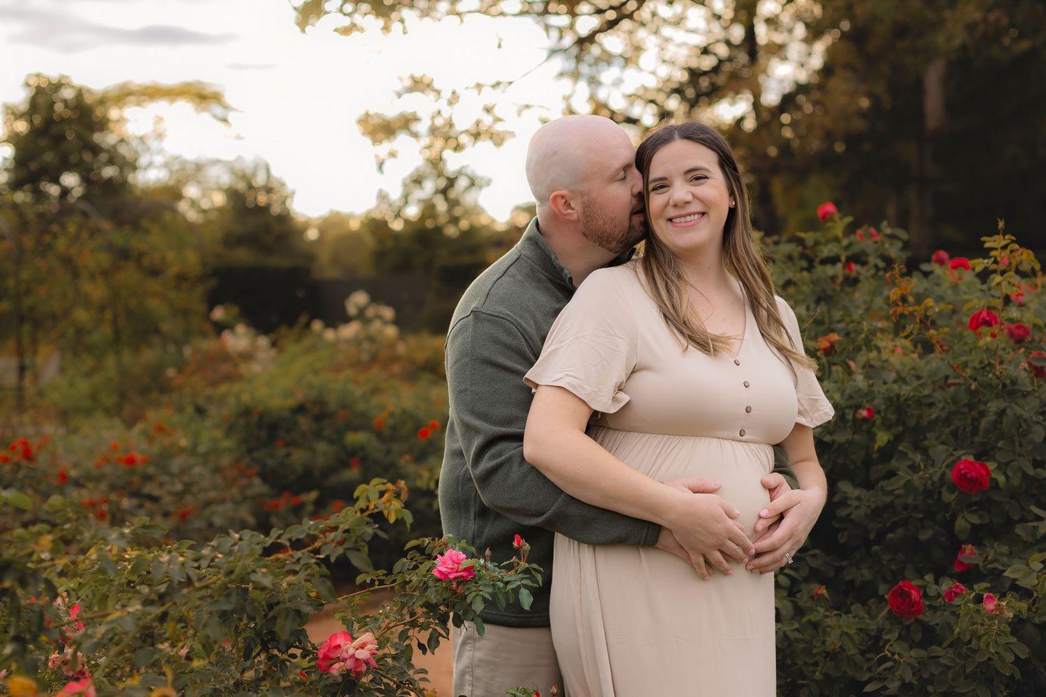 Romantic couple embraces in a garden setting with blooming roses and autumn foliage.
