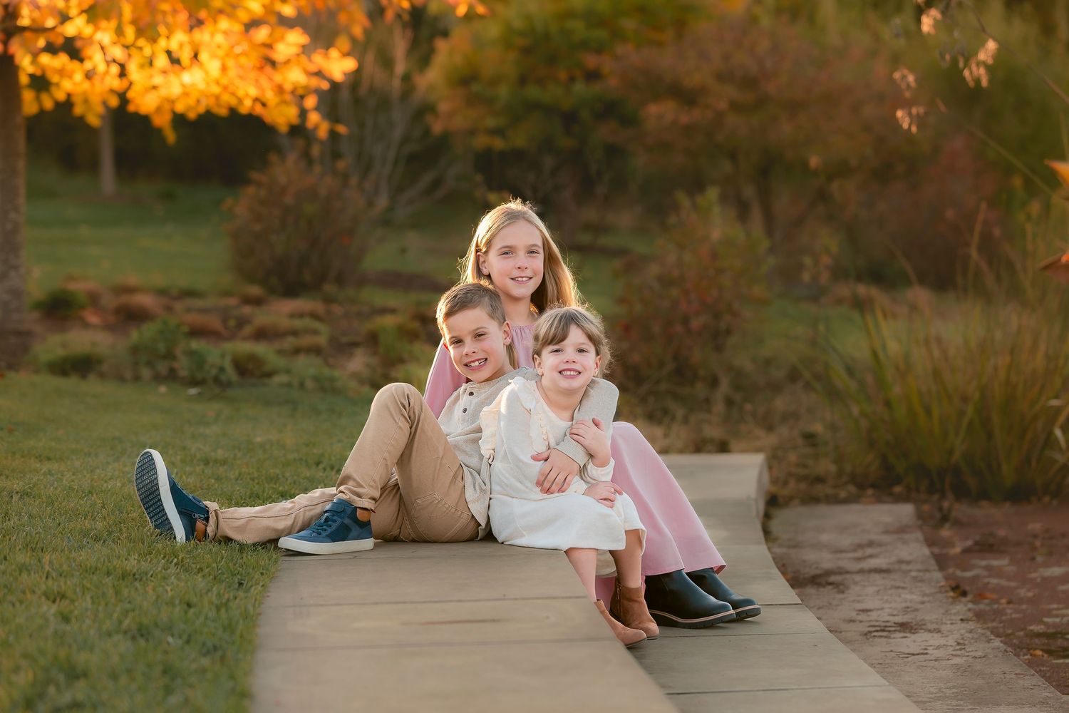 Family members lying on grass during golden hour sunset photoshoot in autumn park.