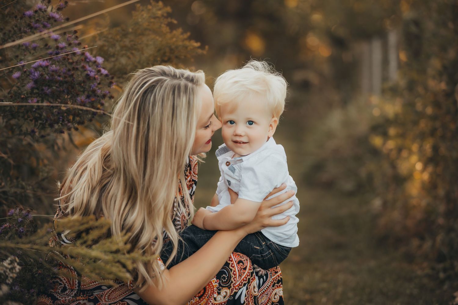 A tender outdoor family photoshoot in warm autumn lighting with natural foliage in the background.