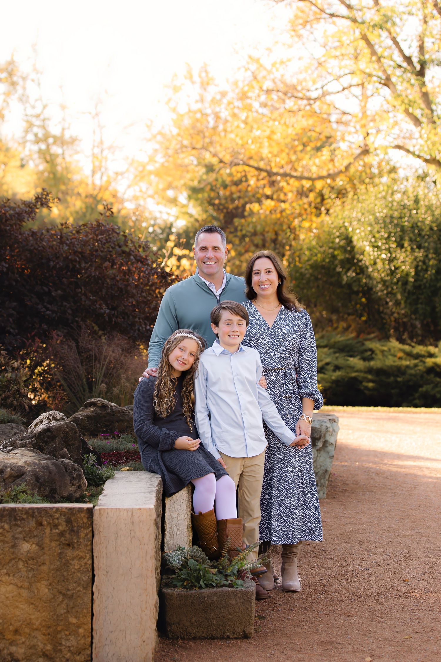 A family sits together on stone blocks along a dirt path surrounded by autumn foliage at golden hour.