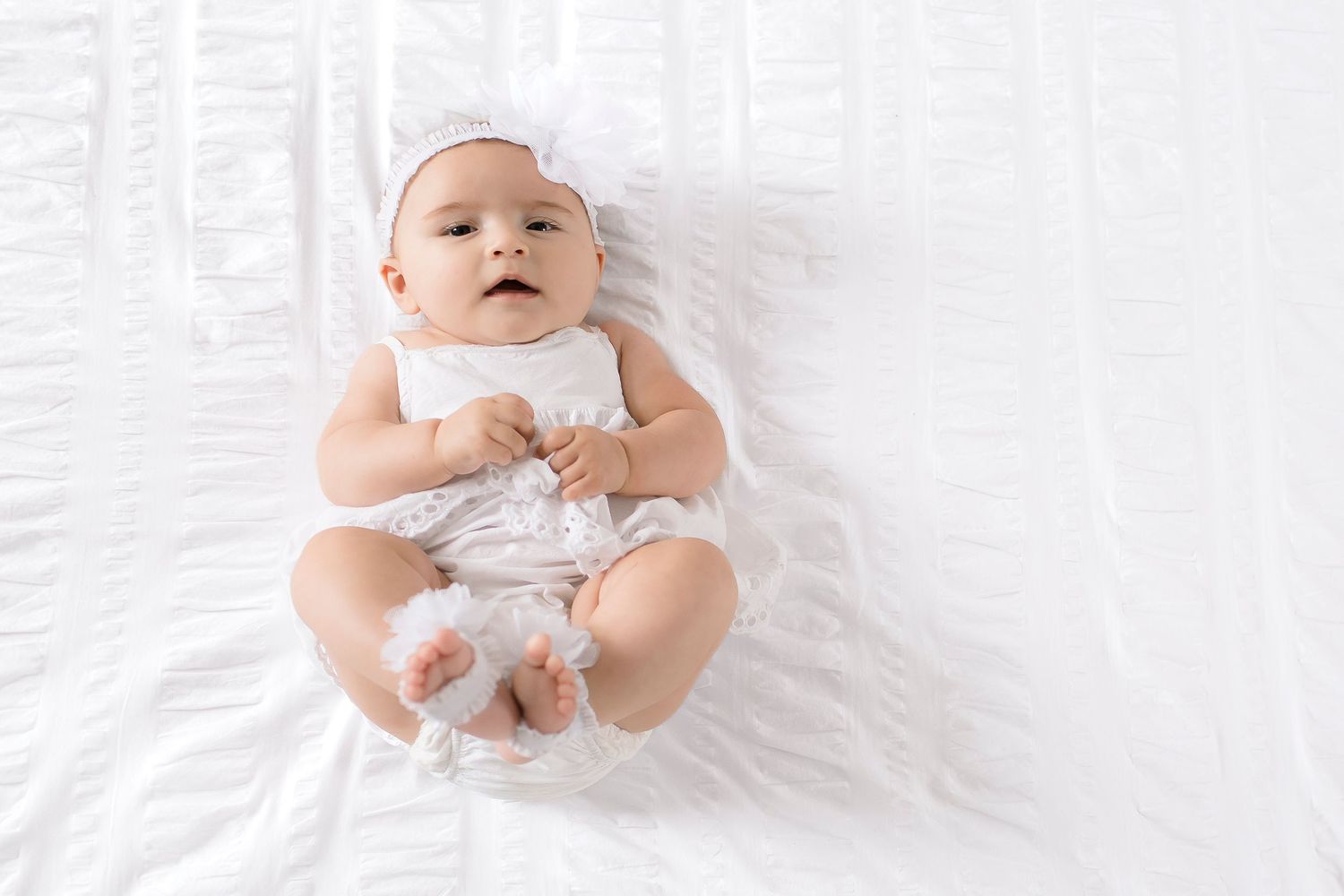 Baby in white onesie lying on white blanket with arms and legs spread out in four different poses.