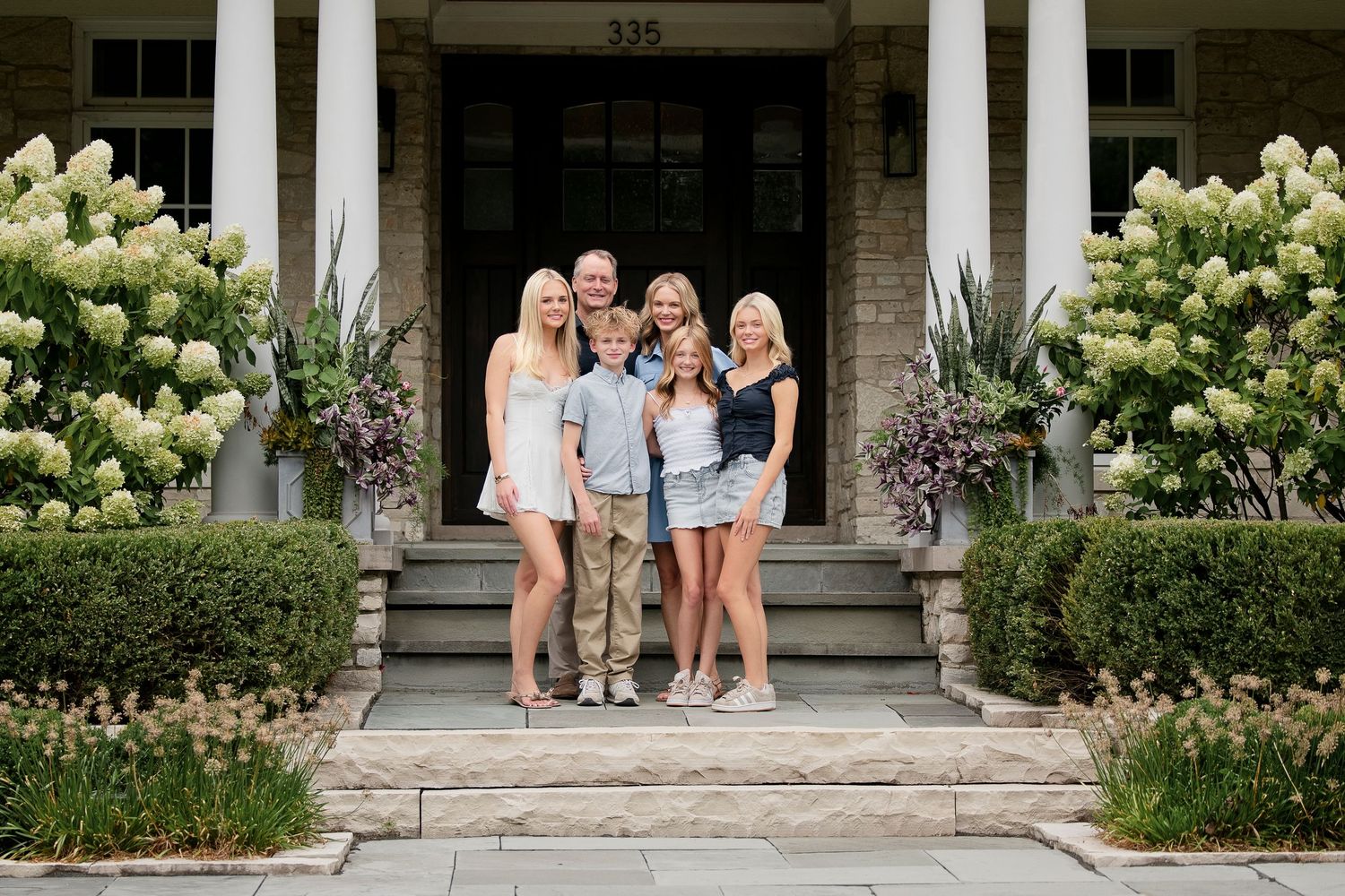 Family of five posing on front steps of elegant home with white hydrangeas.
