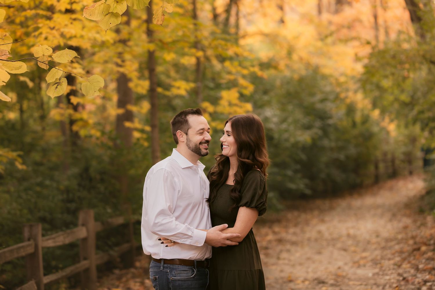 A couple shares a romantic moment on a sunlit forest path surrounded by golden autumn foliage.