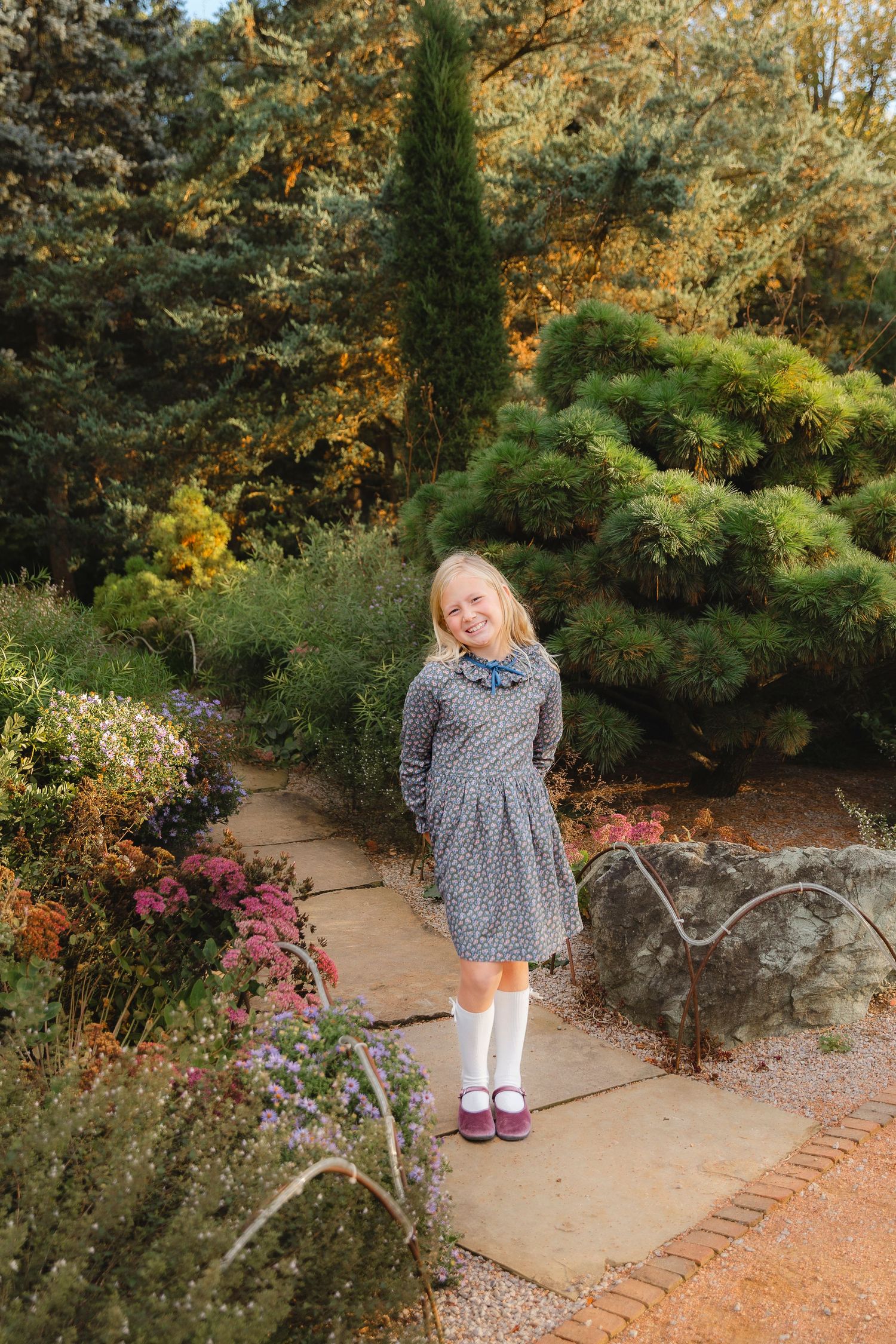 A winding garden path through autumn foliage leads to stone steps surrounded by colorful blooming flowers.