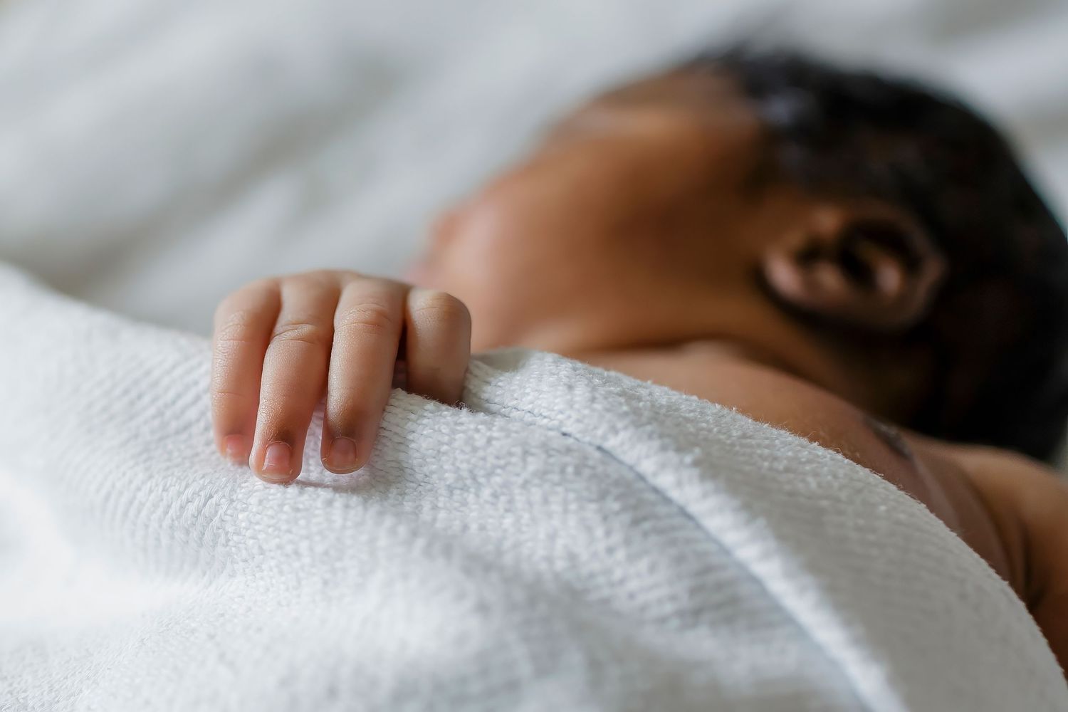 A sleeping newborn baby wrapped in soft white blankets rests peacefully.